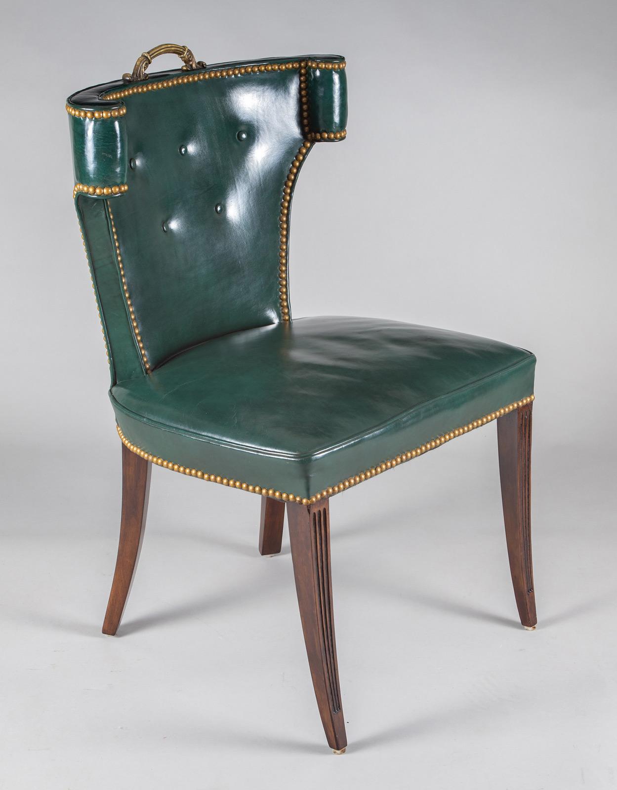 Vintage green leather side or desk chair with a curved and scrolled “semi-wing” back, a brass handle affixed at the top, the leather back with five buttons, tight seat, the unusual design outlined with brass nail heads, supported on fluted mahogany