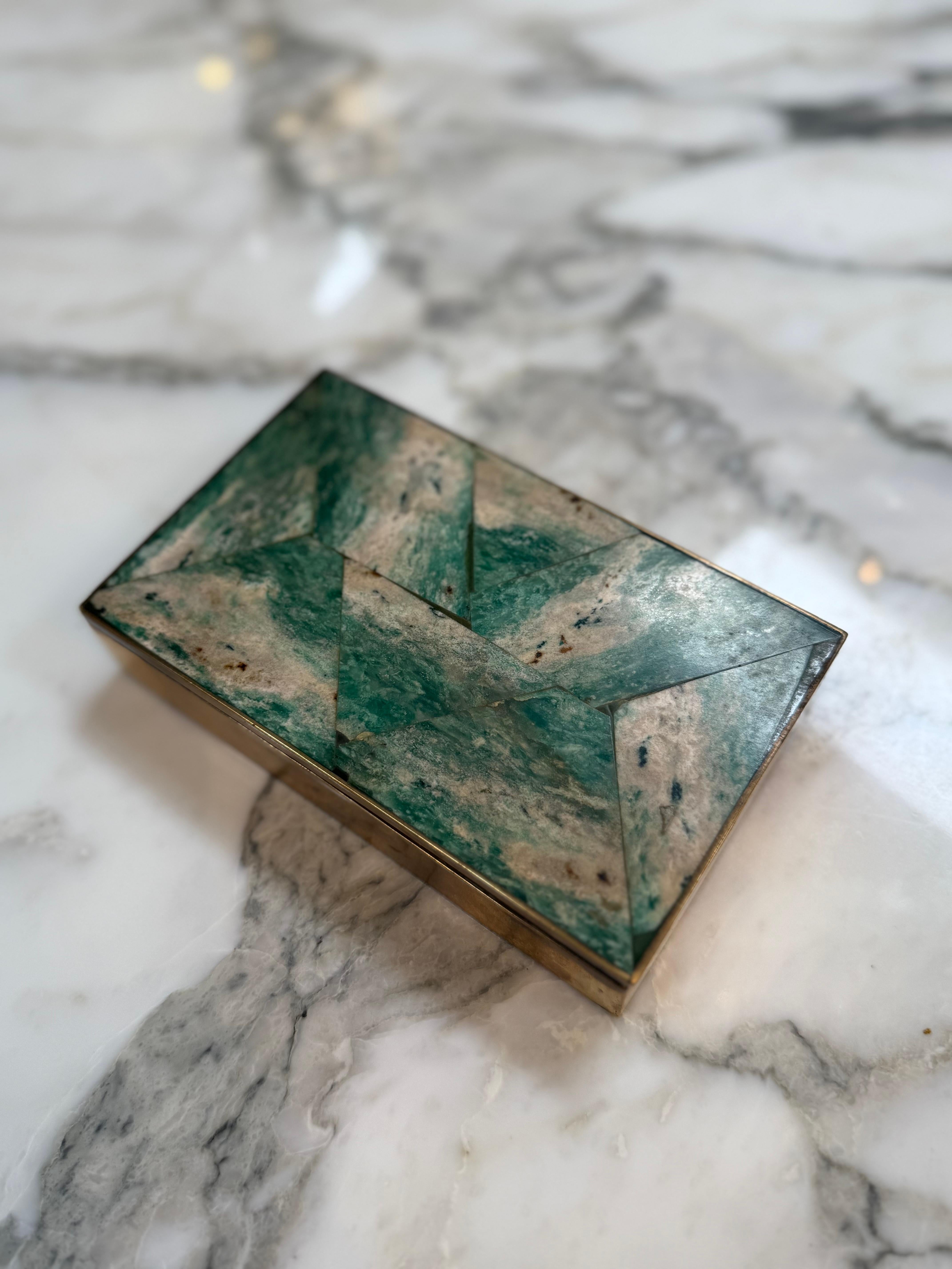 Questo portagioie vintage rettangolare presenta un elegante disegno geometrico a intarsio realizzato con marmo verde o malachite incastonati in una cornice di ottone. Il top presenta un motivo in stile chevron con toni naturalmente variegati di