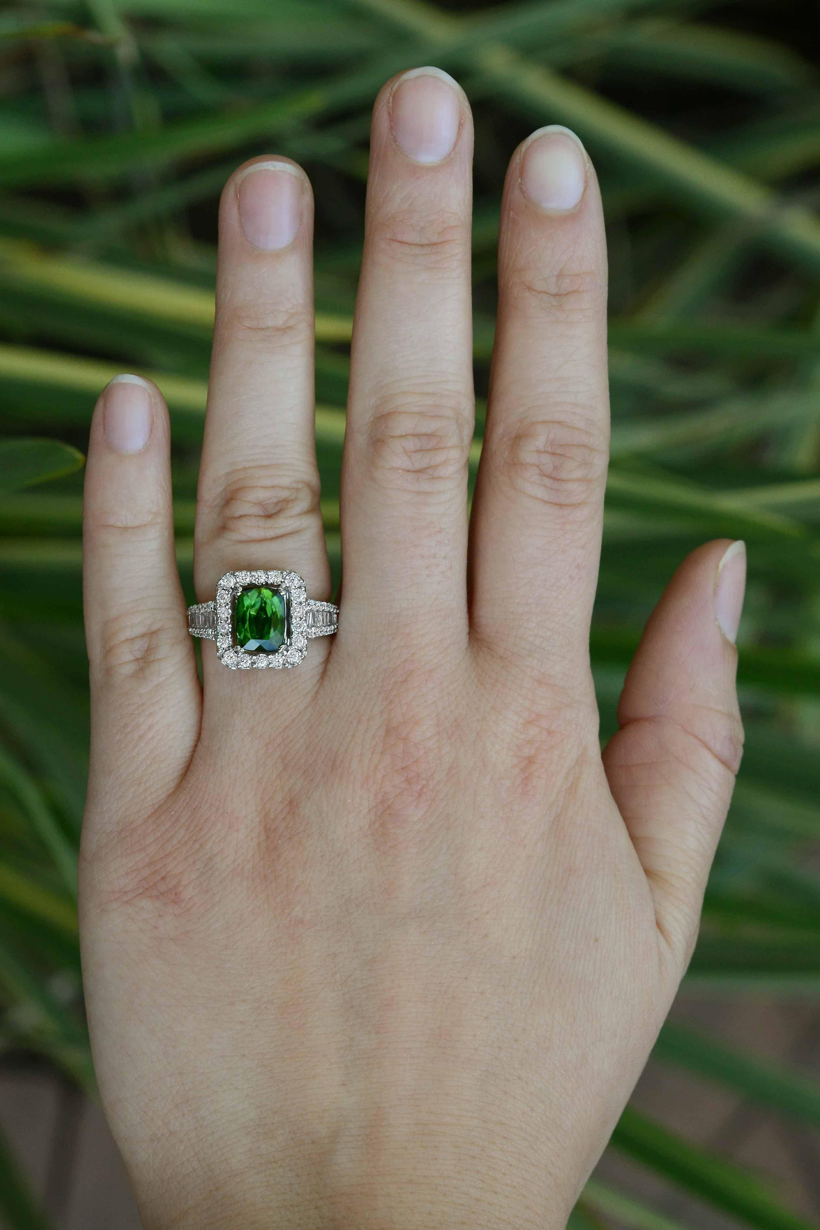 A vivid green tourmaline set in a ravishing diamond embedded white gold setting. The gem displays a rich, forest-green color that beams off your hand. The rectangular halo of glimmering diamonds as well as the cascading composition of baguette and