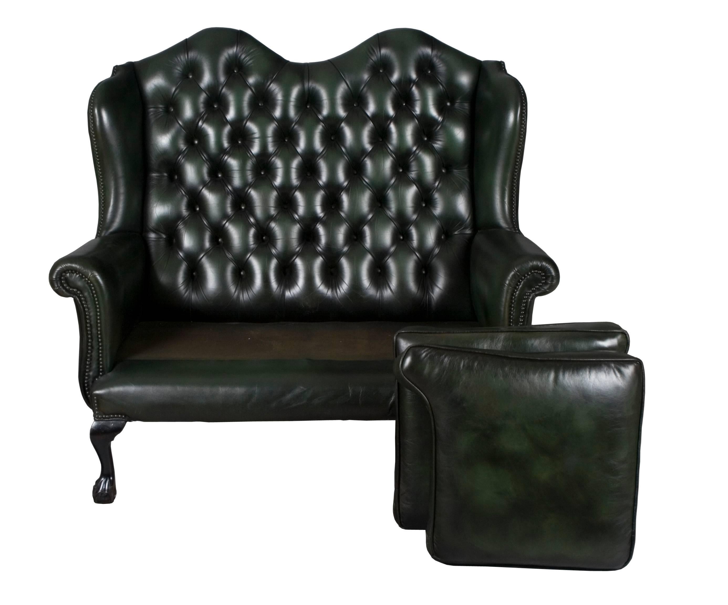 Hailing from England, this tall back leather love seat is stunning and full of charm. Crafted back around 1980 out of a top grade green leather, it remains in very good condition today. Charming leather, a tufted wing back, and Queen Anne style feet
