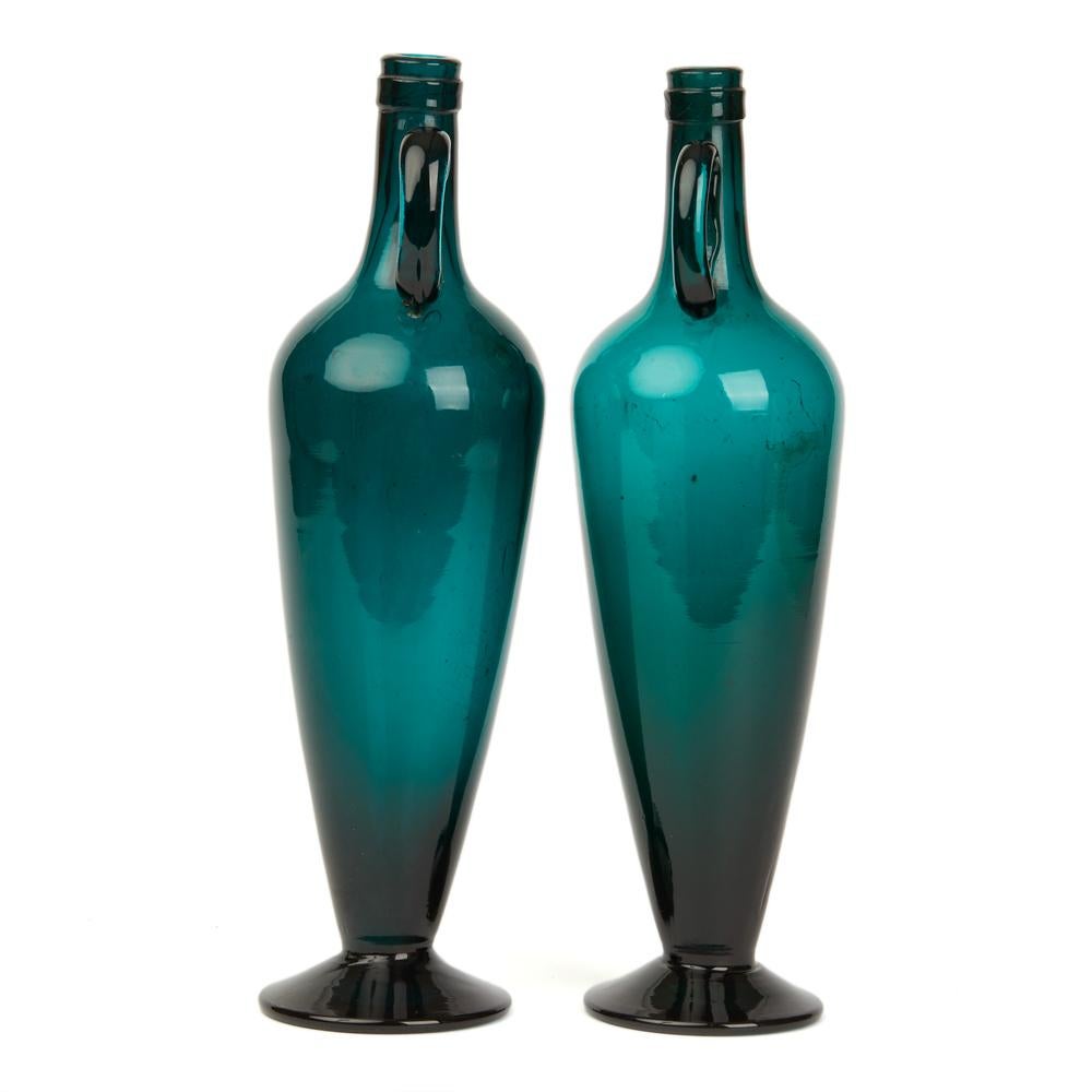 A stylish pair vintage twin handled tall green or turquoise glass bottle vases standing on rounded bases with long graduated bodies and narrow bottle shaped tops with loop handles applied to either side. The vases are not marked.