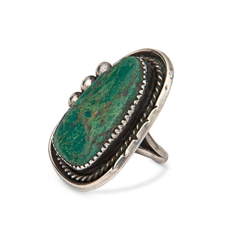 This vintage sterling silver ring features a green turquoise natural stone accented by braiding details and three silver beads on one side. It is set on a double shank. This ring is a size 5.75 but can be resized for a small fee. It weighs 12.8