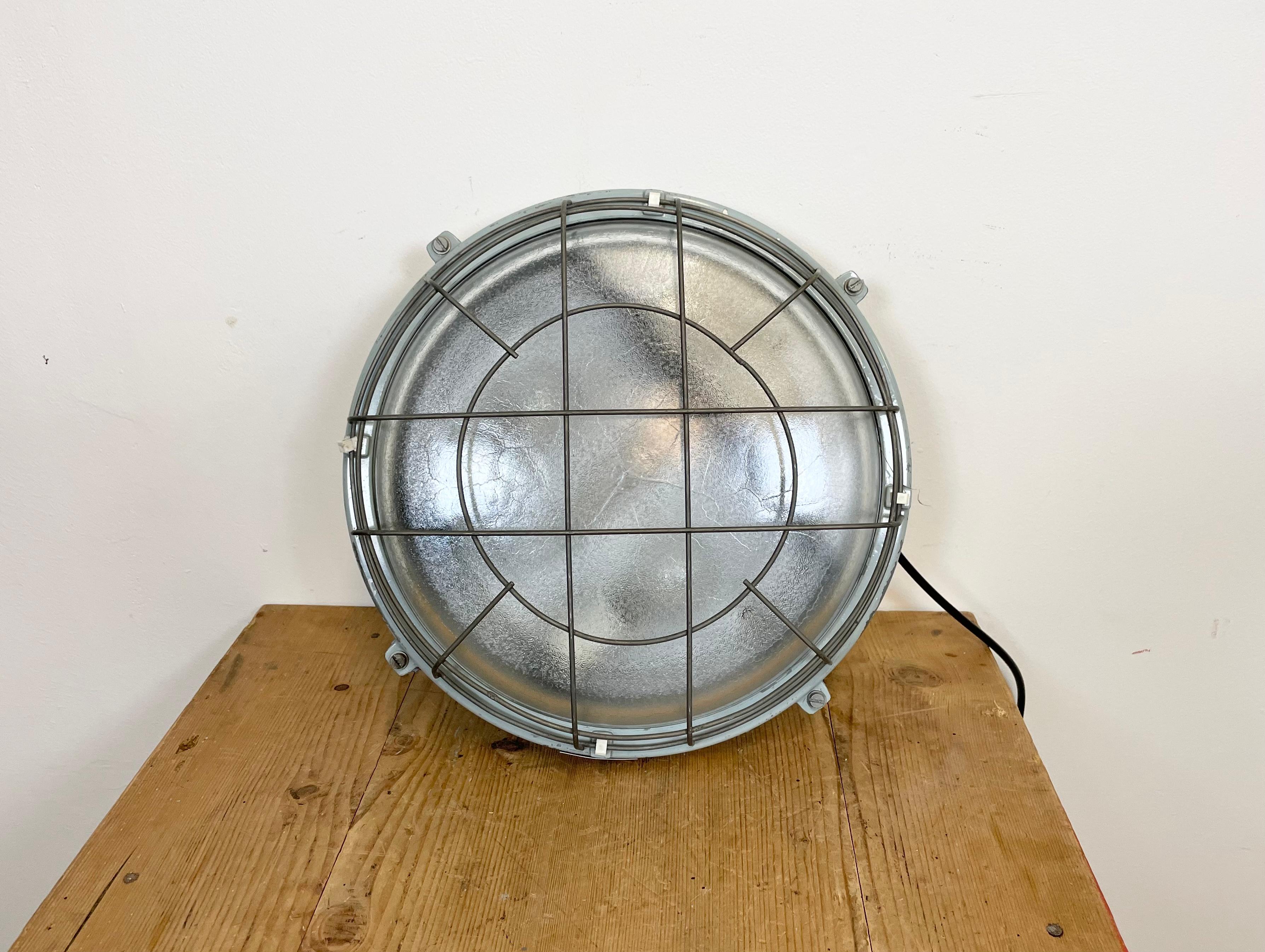This grey cast aluminium wall lamp was made by Elektrosvit in former Czechoslovakia during the 1980s. . It fetures a cast aluminium body, frosted curved glass cover and iron grid. Two porcelain sockets require E 27 light bulbs. It can be also used