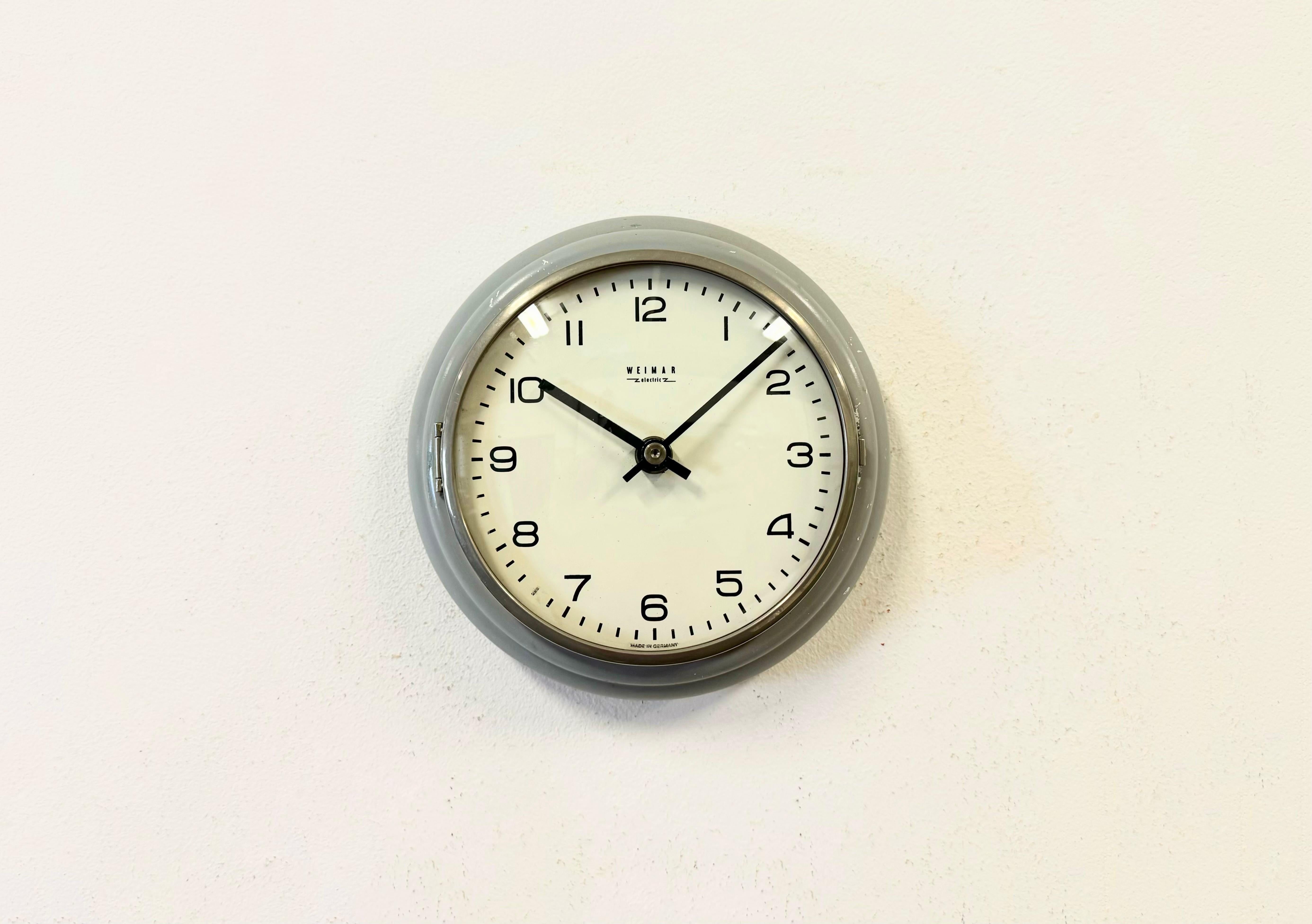 Vintage Industrial wall clock produced by Weimar Electric in former East Germany during the 1970s. It features a grey iron frame, a metal dial, an aluminium hands and a curved clear glass cover. The original battery-powered clockwork requires one C