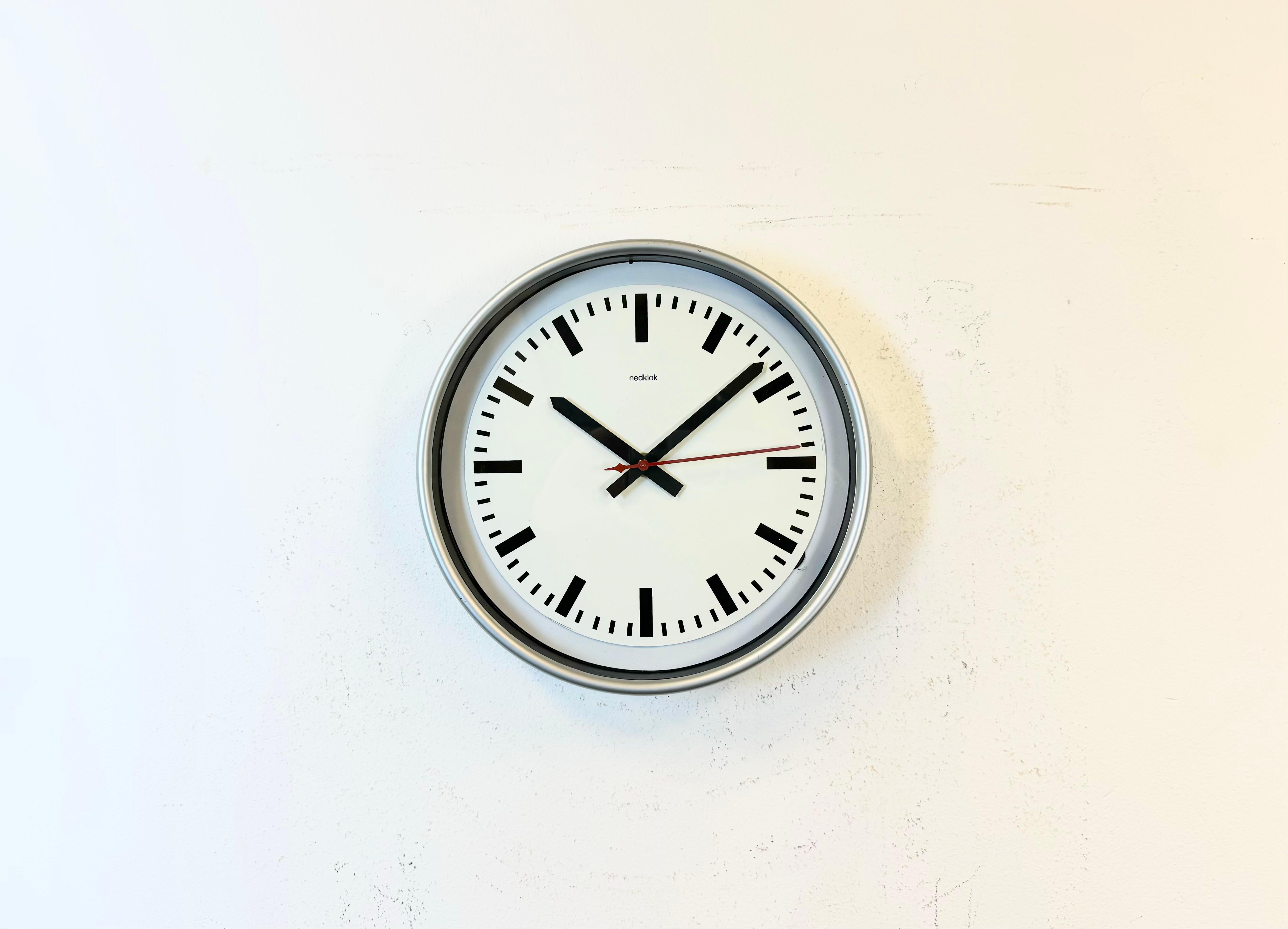 Nedklok wall clock was made in Netherlands during the 1990s. It features a grey ( silver ) plastic frame, a metal dial, an aluminium hands, and a clear glass cover. Original electric movement ( 220 V ) works perfectly . The diameter of the clock is