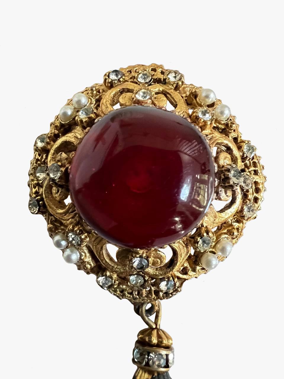 Wunderschöne Vintage-Brosche aus Gripoix-Glas, die auch als Anhänger verwendet werden kann. 

Nicht unterzeichnet.

Ein dunkelroter Cabochon ist in einen goldfarbenen Metallrahmen mit Strasssteinen und Perlen eingefasst. 

Zustand - sehr gut,