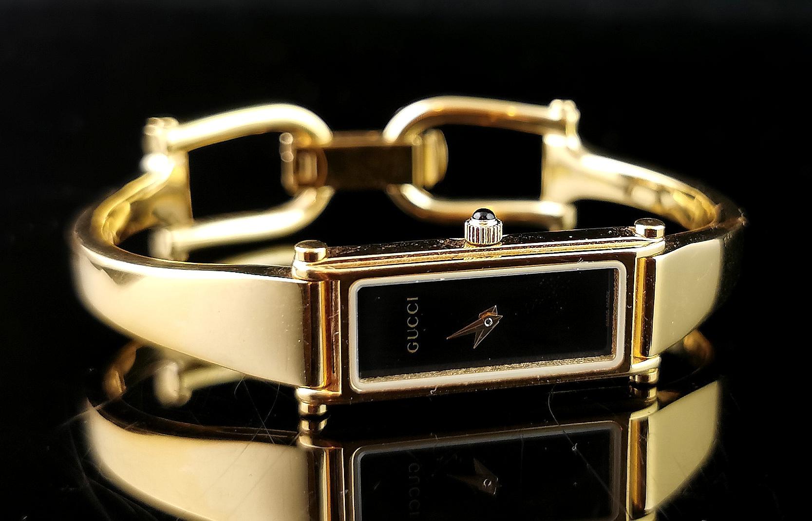 A stylish Gucci 1500l ladies gold plated wristwatch.

This is a bracelet or bangle strap watch with a nice sleek gold plated bangle strap with the signature Gucci horsebit clasp.

The case is gold plated with a black dial, no numerals and Gucci