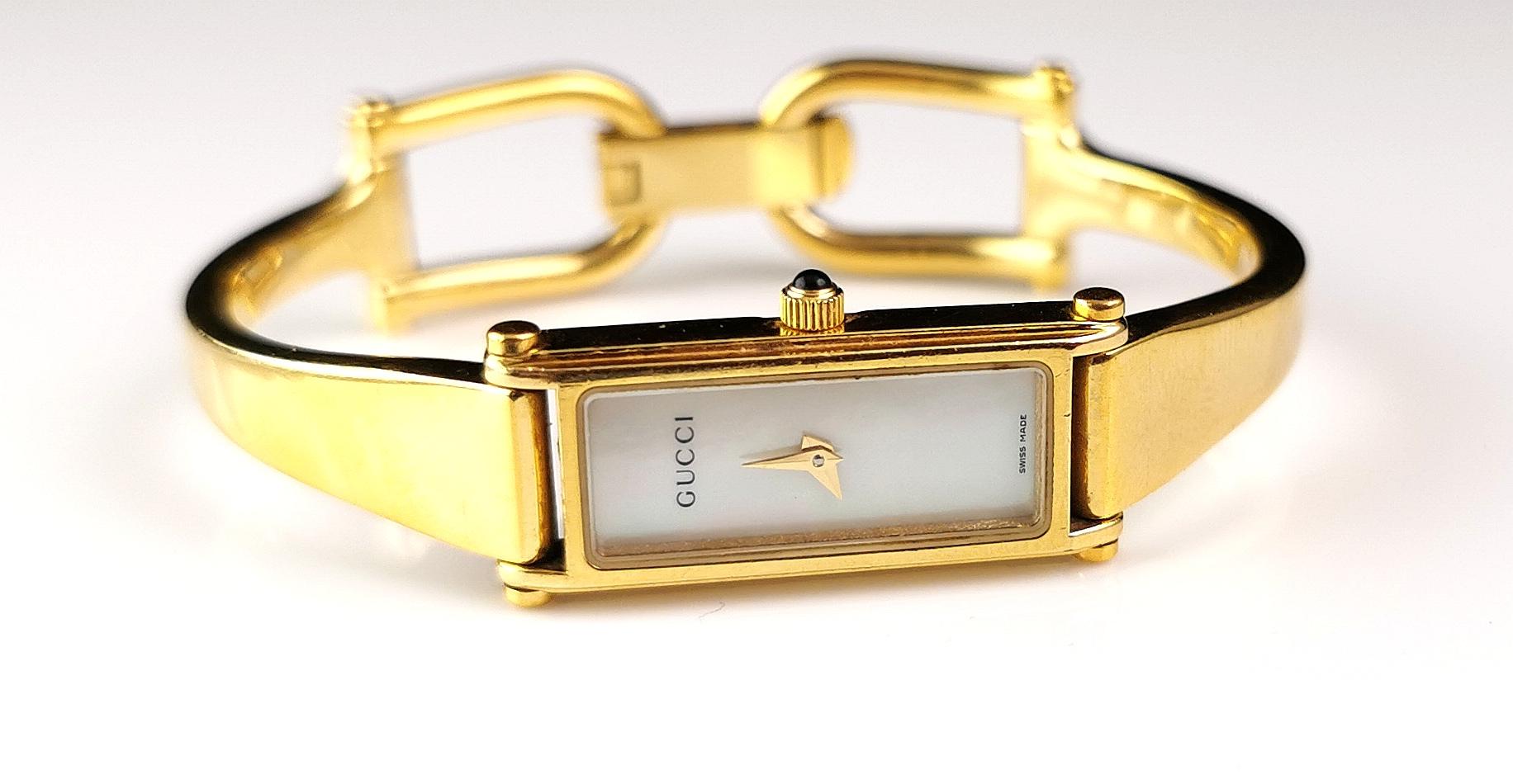 A stylish Gucci 1500l stainless steel watch.

This is a bracelet or bangle strap watch with a nice sleek gold plated bangle strap with the signature Gucci horsebit clasp.

The case is gold plated with an off white dial, no numerals and Gucci logo,