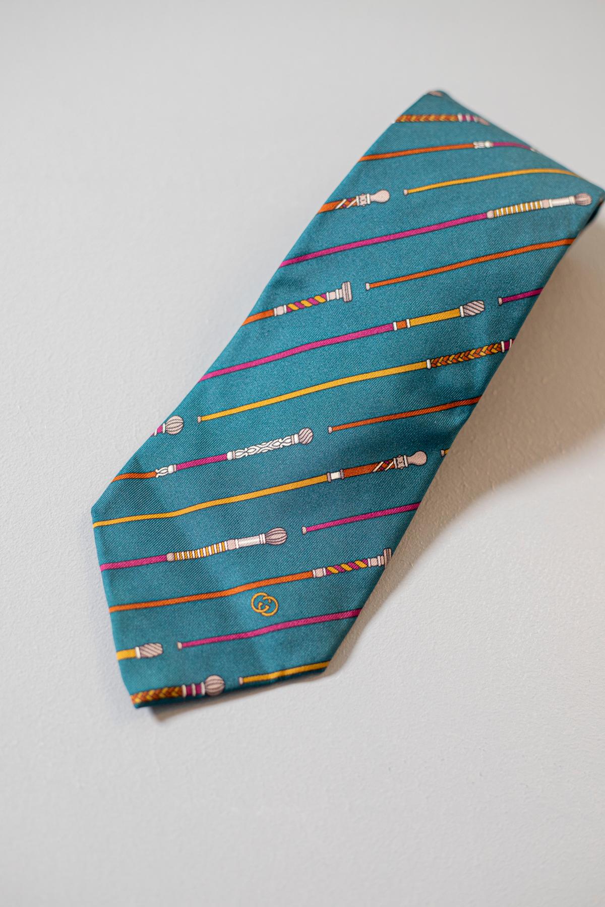Diese von Gucci entworfene Krawatte ist aus reiner Seide gefertigt. Dieses schlichte, aber elegante Accessoire zeigt bunte Spazierstöcke auf quetzalgrünem Hintergrund. Diese Krawatte ist perfekt für jede Gelegenheit, da sie stilvoll und
