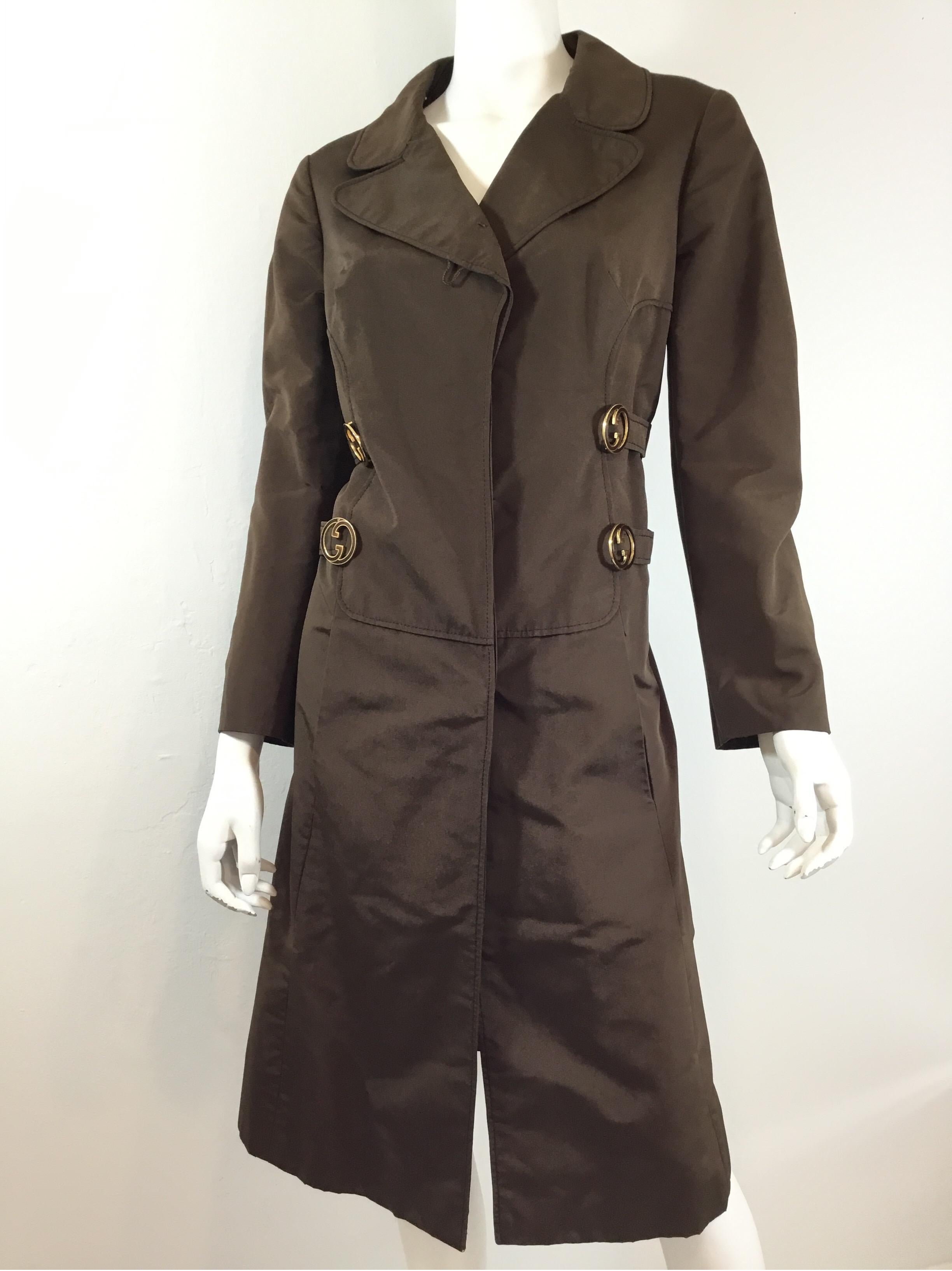 Vintage Gucci jacket featured in brown with concealed button closures along the front, decorative straps along the side with gold tone metal insignia. Jacket has pockets at the waist and is fully lined, composed of 100% waterproof silk. Made in