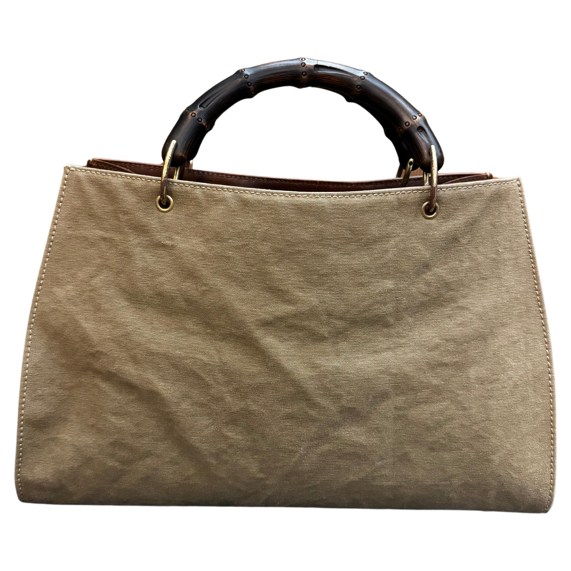 This vintage GUCCI bamboo tote is crafted of canvas in khaki and smooth calfskin leather in brown featuring gold toned hardware and sturdy bamboo handles. Wide top opens to a zippered compartment in the middle and two open compartments featuring a