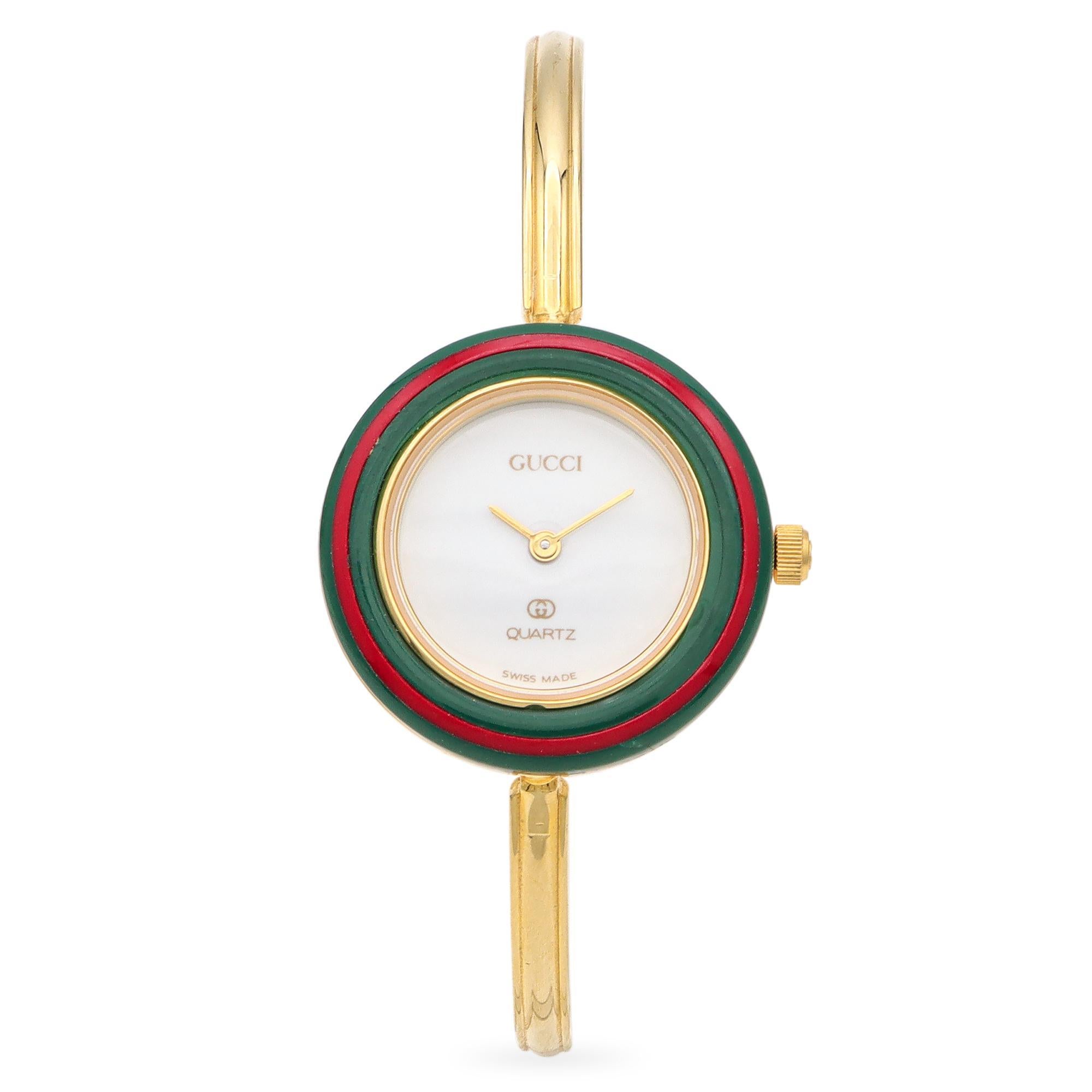 This Gucci watch features a sleek gold-plated bangle design. The round face is encased in a vibrant interchangeable bezel, offering a variety of colors for customization. The minimalist dial is marked with simple indices and the Gucci logo. The