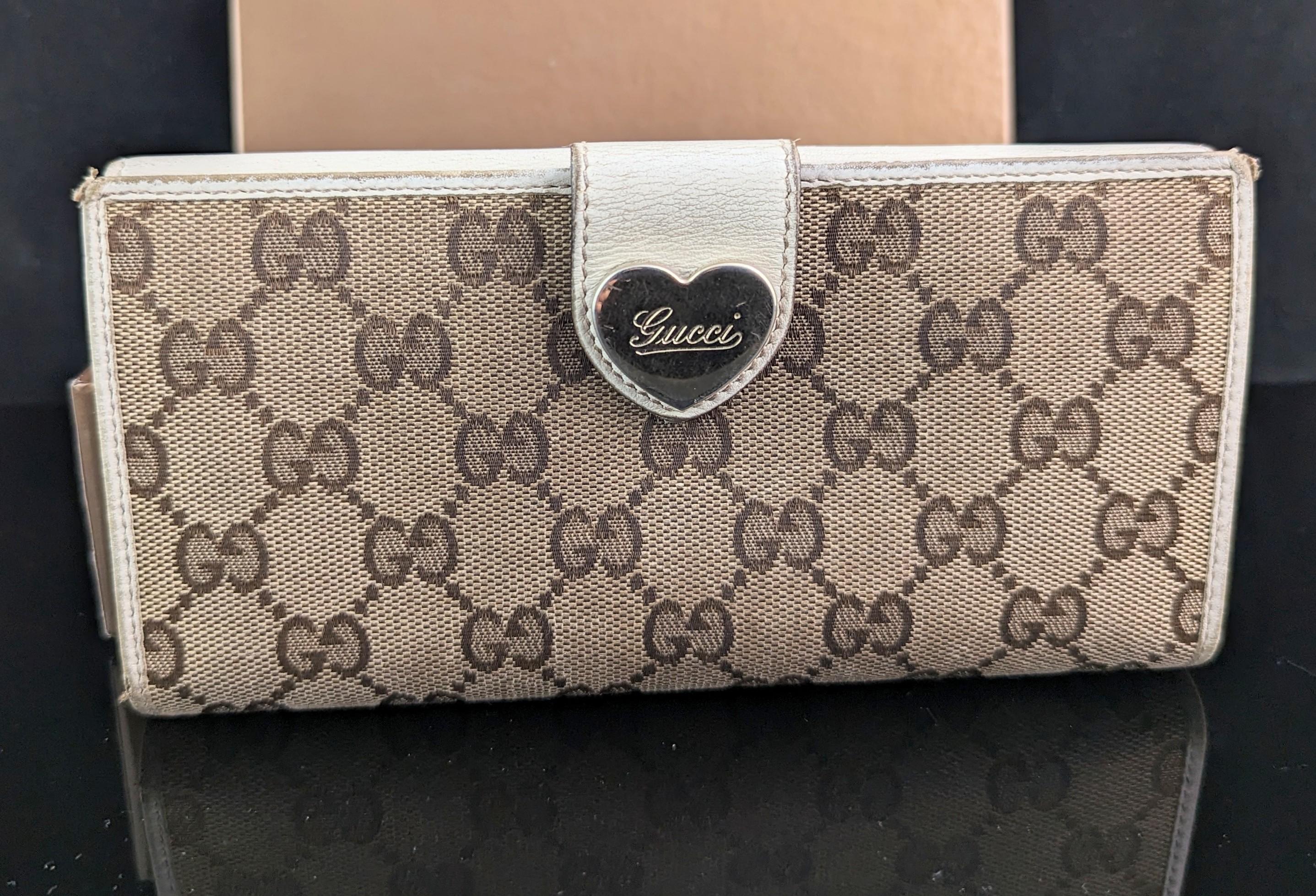 An Iconic vintage early 2000s ladies Gucci GG monogram purse.

This is a signature monogram canvas covered larger size purse with cream leather and gold tone metal hardware including a gold heart metal clasp.

The purse has multiple internal