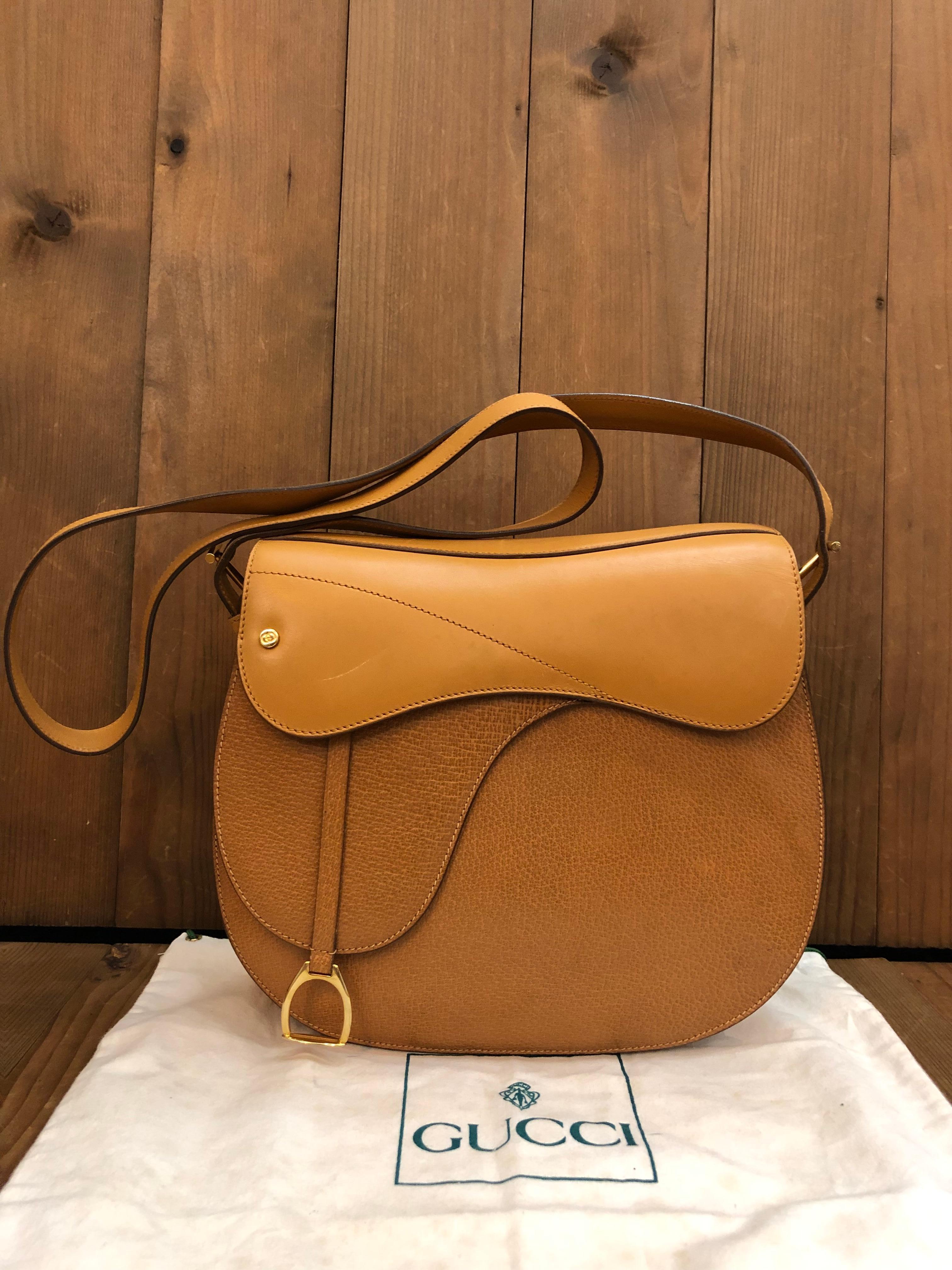 This 1980s vintage GUCCI saddle bag is crafted of smooth calfskin and pigskin leather in camel featuring gold toned hardware. Front magnetic snap closure opens to a beige leather interior featuring a zippered pocket. Made in Italy. Measures