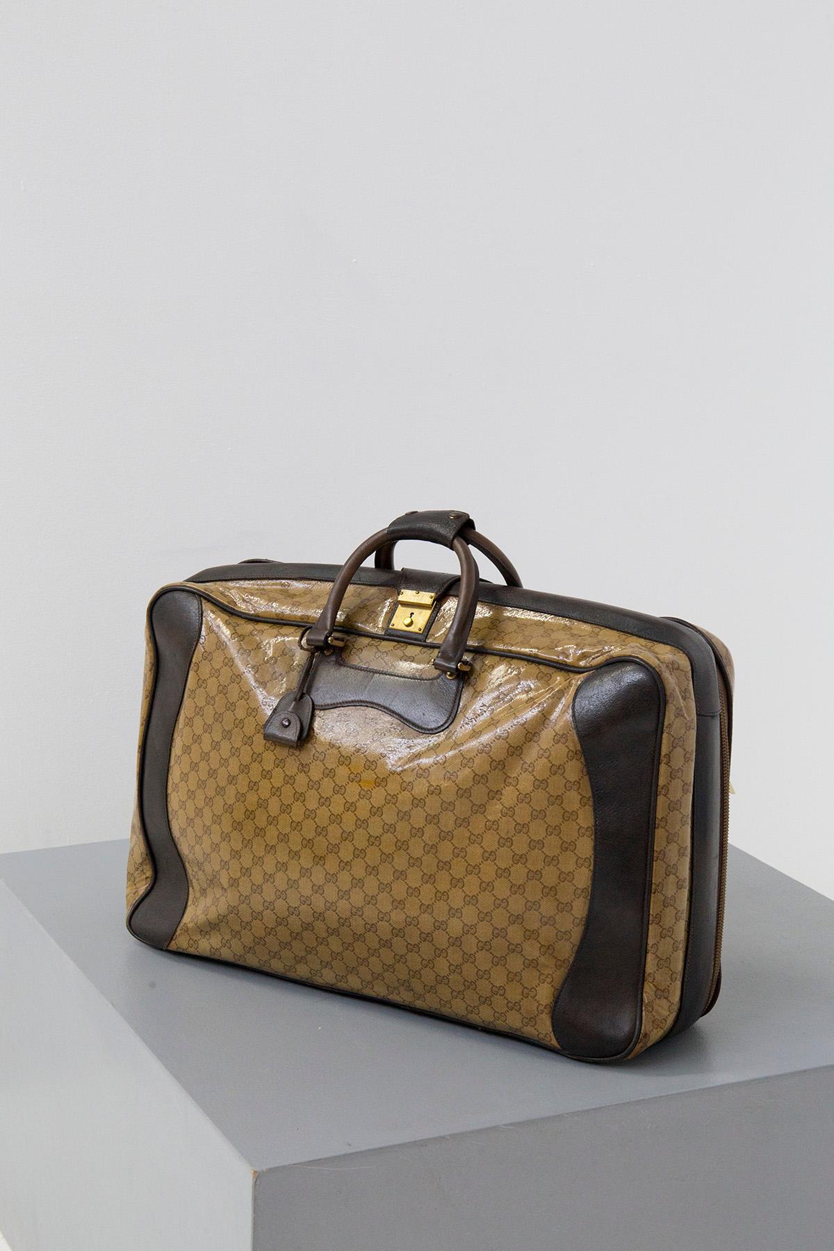 Élégant sac de voyage signé Gucci, datant des années 1970-80. Fabriqué avec du cuir brun figir. L'ensemble du sac arbore son logo original dans un cuir acétate beige très souple. On remarque deux poignées en cuir très élégantes qui permettent de