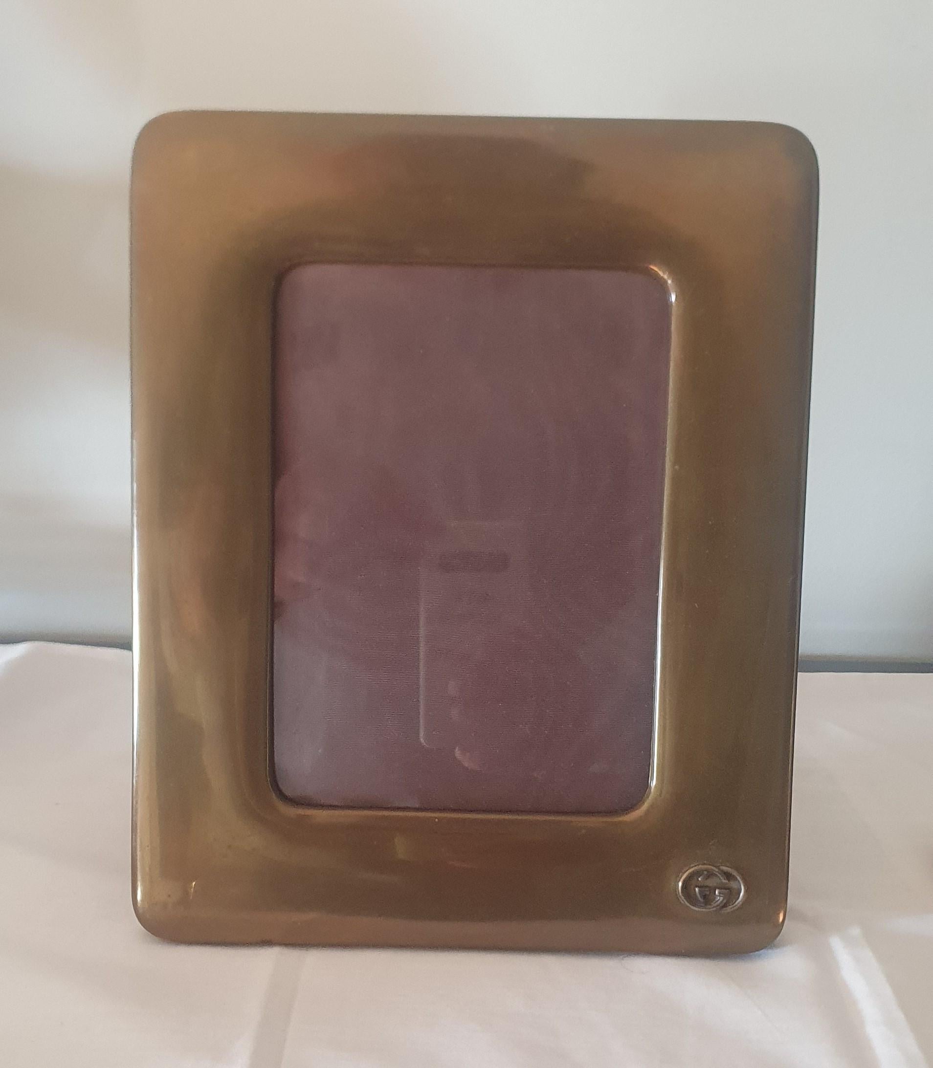 This is a beautifully thick luxurious photograph frame by the world renowned house of GUCCI

Made of Brass, it consists of a wide and deep cushioned effect moulded metal frame mounted on to a thick plush chocolate brown Velvet back with hinged leg