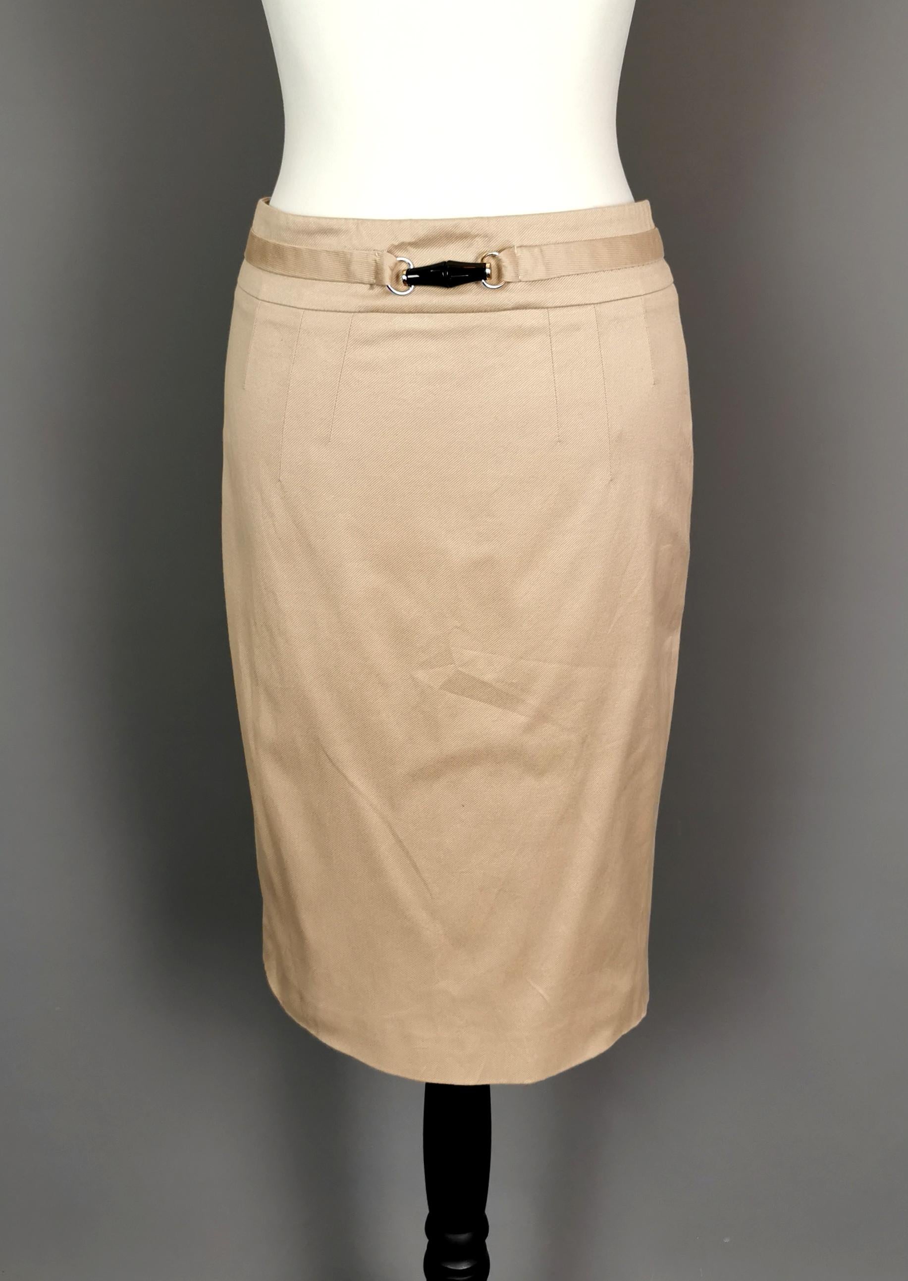 A stylish vintage Gucci, Tom Ford era pencil skirt.

It is made from a warm dark beige or sand colour with a bamboo trim at the waist in gold tone metal and black plastic.

The skirt has a split hem at the back and a pencil silhouette, perfect for