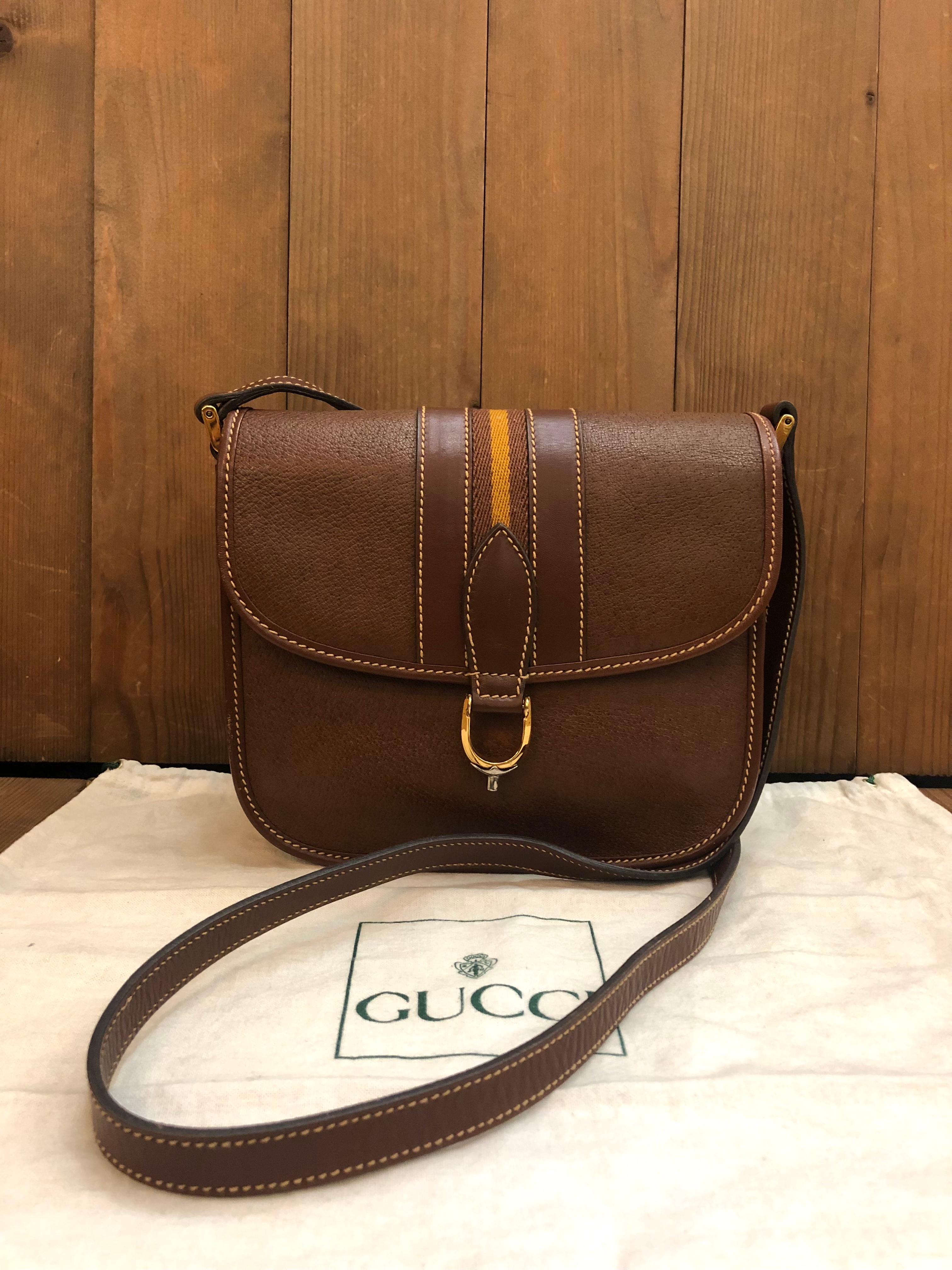 This vintage GUCCI Web equestrian crossbody bag is crafted of pigskin leather in brown featuring gold toned hardware and decorated with a brown/yellow stripe. Front magnetic snap closure opens to a brown nubuck leather interior featuring two open