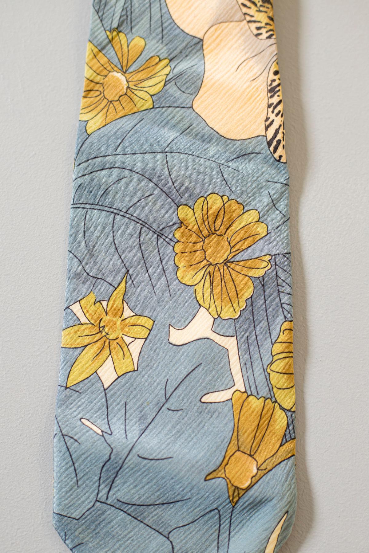 Made in Italy and designed by the French stylist Guv Laroche, this tie is classy and fine. It is decorated with yellow flowers and blue leaves on a beige background. This all-silk tie is fresh and perfect for an elegant occasion or for a quiet