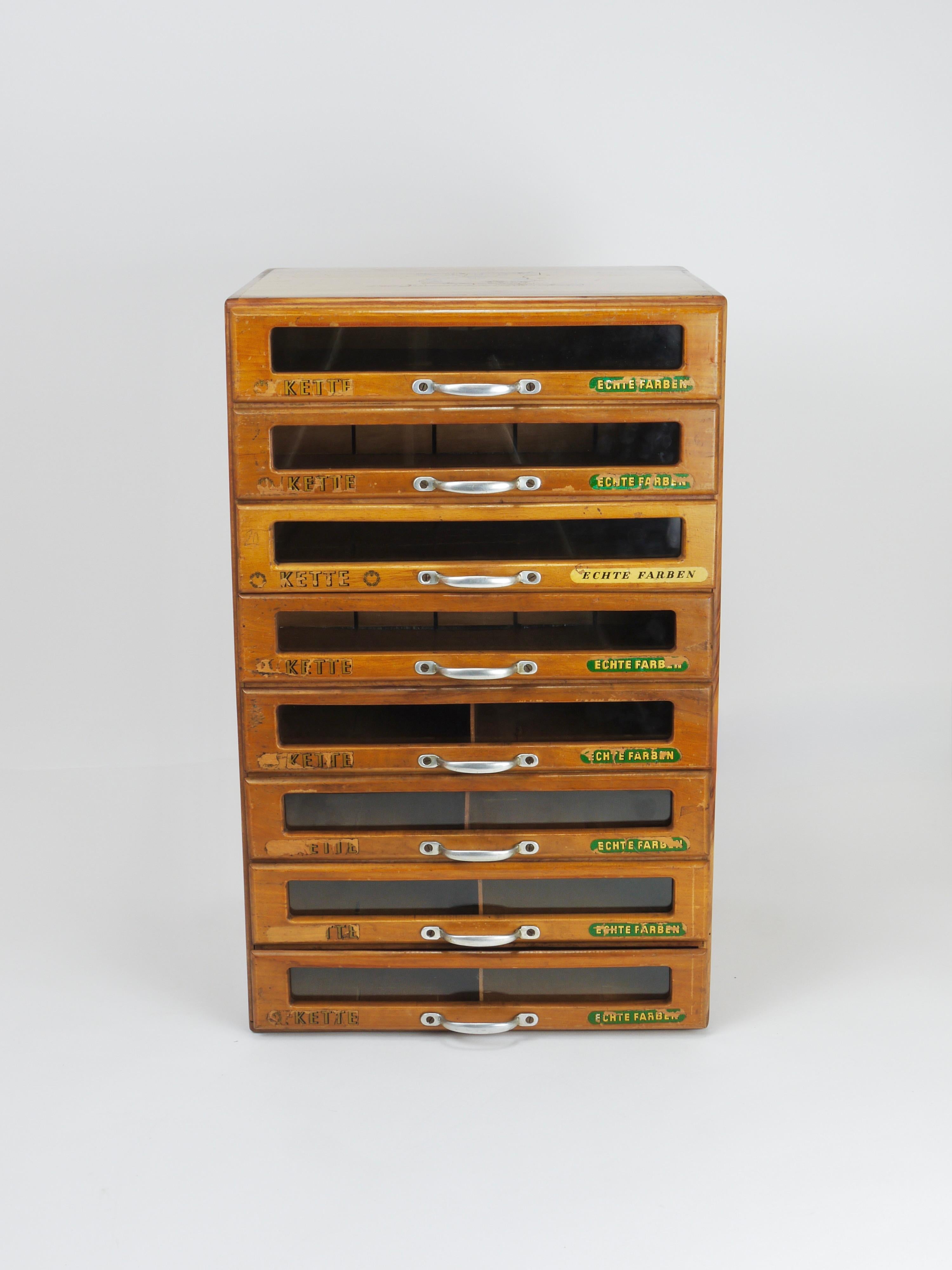 Un bellissimo espositore da banco per merceria in stile industriale / cassettiera o mobile per riporre il filo da cucito o il filato degli anni '30. Realizzato in legno, presenta otto cassetti con maniglie in metallo, realizzati per Kette /