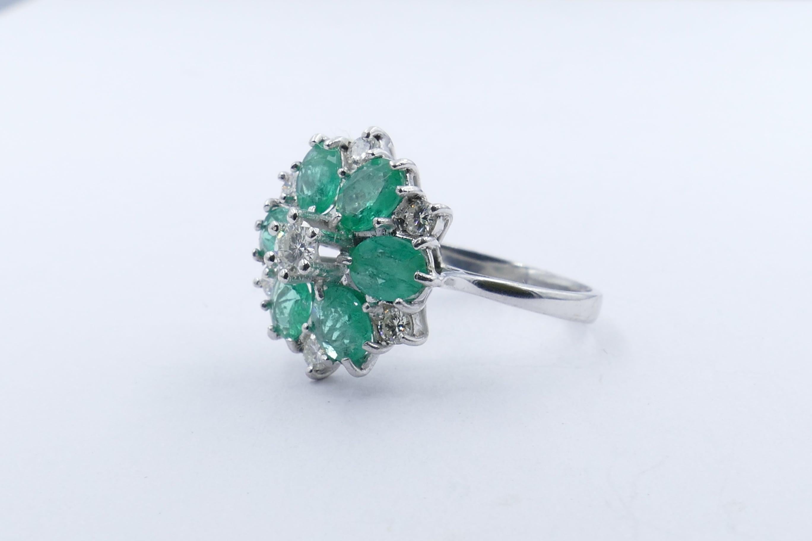 A pretty little Diamond, colour H-J, clarity VS2, 6 claw set is the centrepiece of this lovely Vintage Flower-like Ring.
Surrounding the Diamond are 6 bright bluish-green Emeralds with another 6 round brilliant cut Diamonds, colour G, clarity