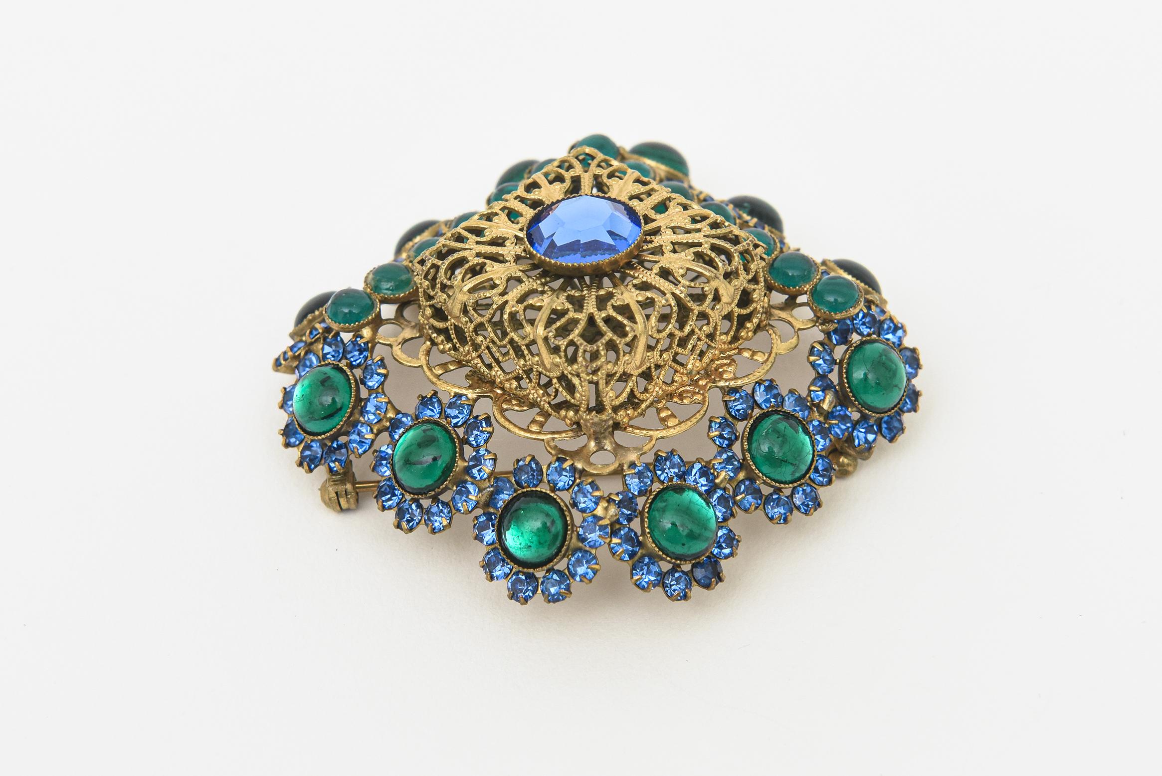 This stunning vintage hallmarked Hattie Carnegie pin/ brooch can be angled or placed straight on. The gilt metal filigree work is surrounded by blue and green glass stones. Signed Hattie Carnegie on the back. This is a rare brooch and we have the