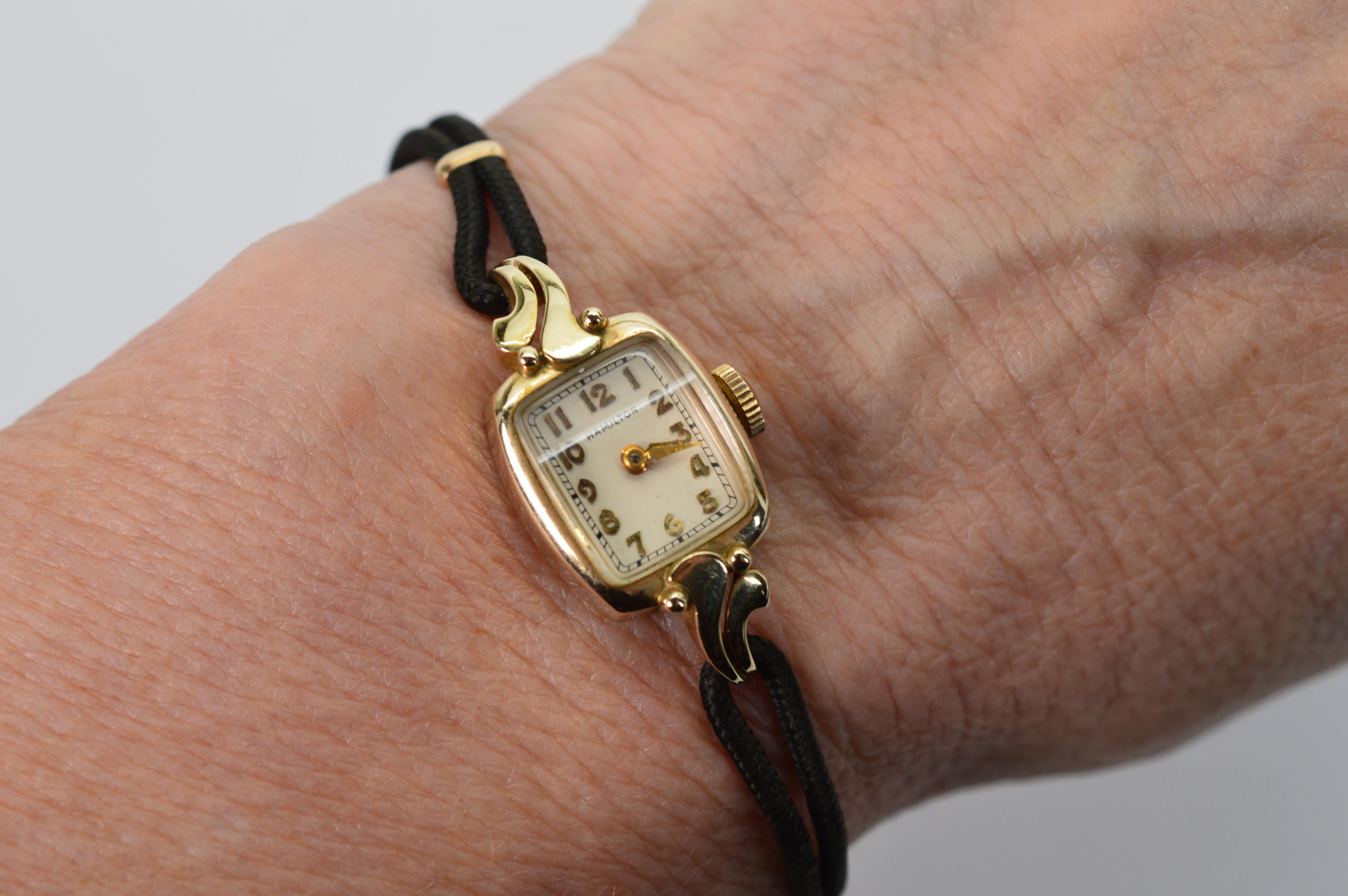 Understated 1950s fashion , enjoy this ten karat 10K Yellow Gold Ladies Hamilton 750  Vintage Watch. Delicate features along with antique imperfections make this a charming piece. Has a 17 jeweled manual wind movement and black Hadley rope bracelet