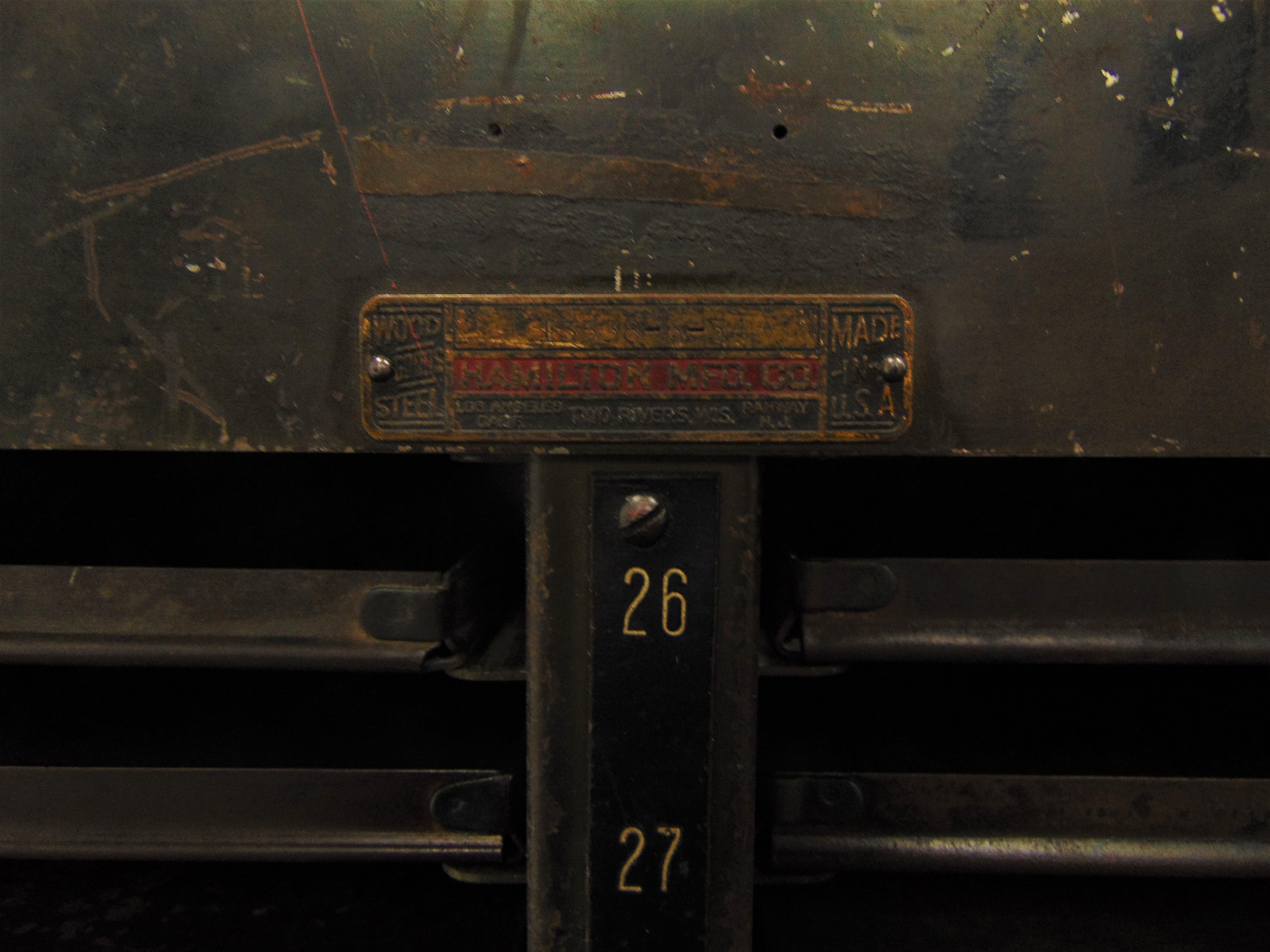 An army green commercial grade vintage steel cabinet by Hamilton. It has great patina and has 46 of its original 50 sliding drawers. All the drawers/trays are in good condition and can be easily removed and moved around. Each drawer slot is labeled