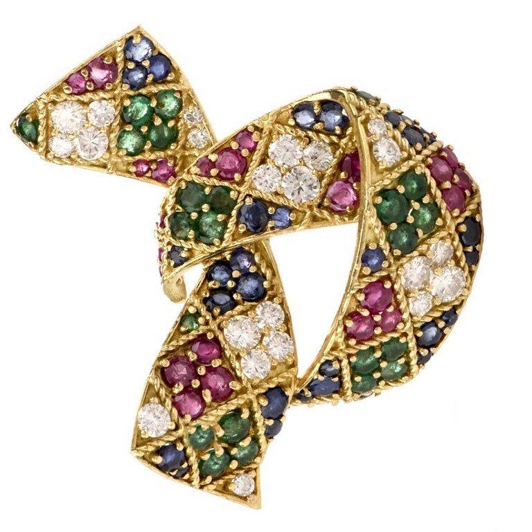 This elegant vintage designer diamond and multi stone brooch is crafted by Hammerman Brothers in 18-karat yellow gold, weighing 31.2 grams and measuring 48mm by 54mm. Simulating a ribbon bow, prong set with 22 round-cut diamonds, collectively