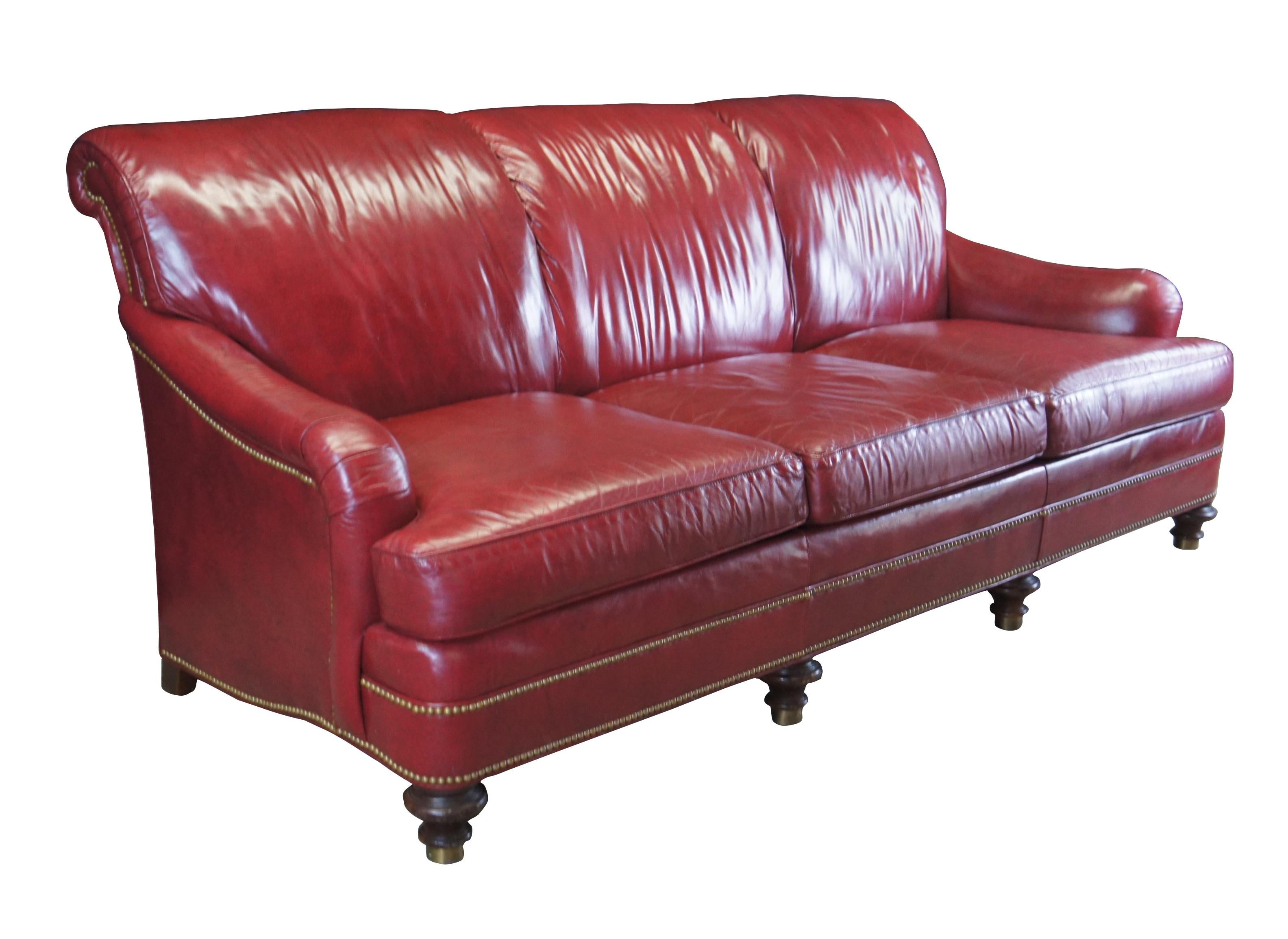 A regal Hancock & Moore Sofa, circa last quarter 20th century. Features a slope arm and scrolled back.  Upholstered in a rich red leather with brass nail head trim.  The sofa is supported by turned mahogany bun feet with brass