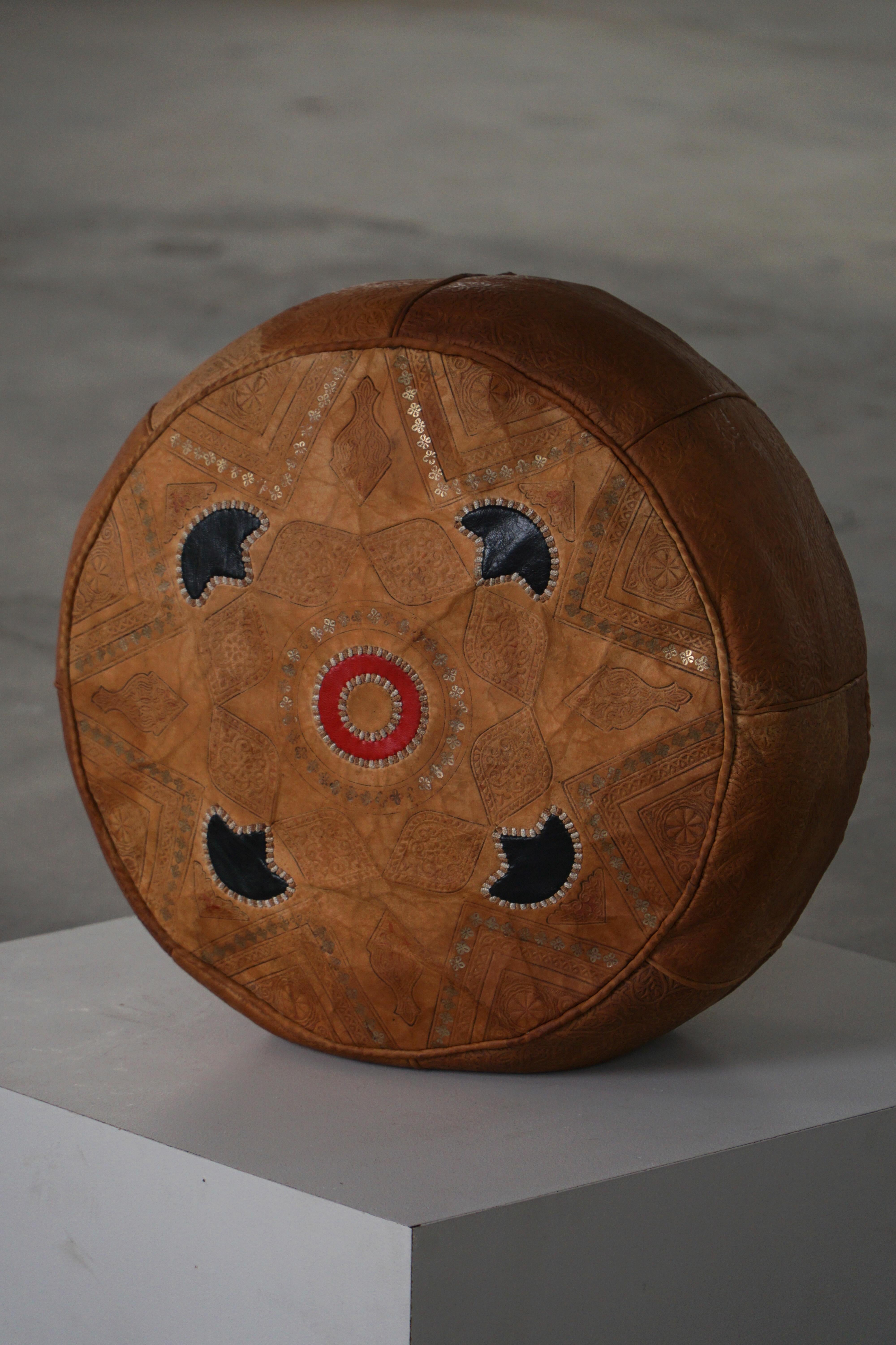 Un magnifique pouf en cuir marocain fabriqué à la main, mettant en valeur un savoir-faire artisanal exquis et un design géométrique. Réalisée en cuir naturel, cette pièce présente des motifs complexes, travaillés à la main et brodés dans des tons