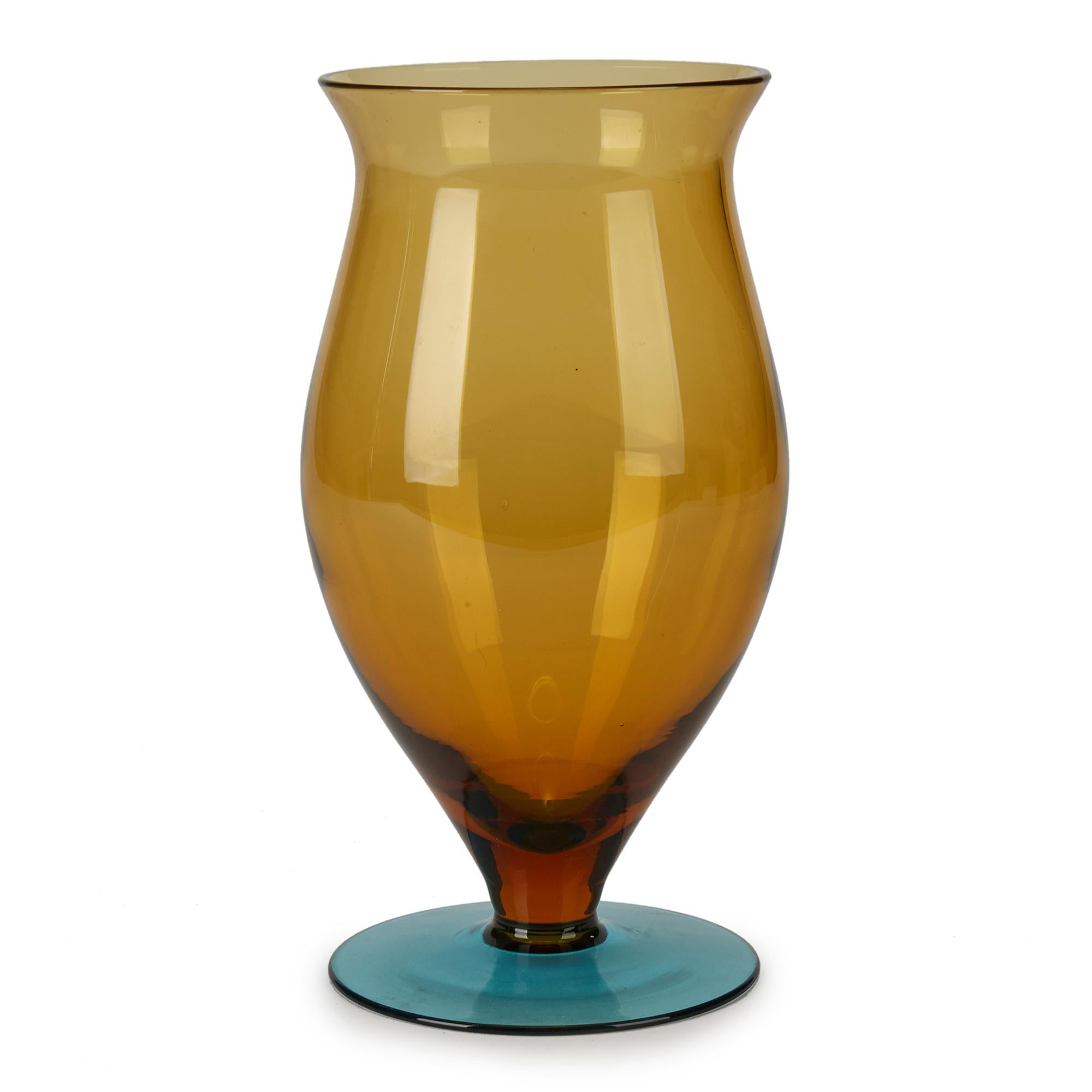 A very stylish vintage hand blown art glass pedestal vase with an amber glass bulbous bud shaped body on a blue glass foot. This stylish vase has the customary handcrafted fine inclusions within the body and is not marked but has wear to the foot