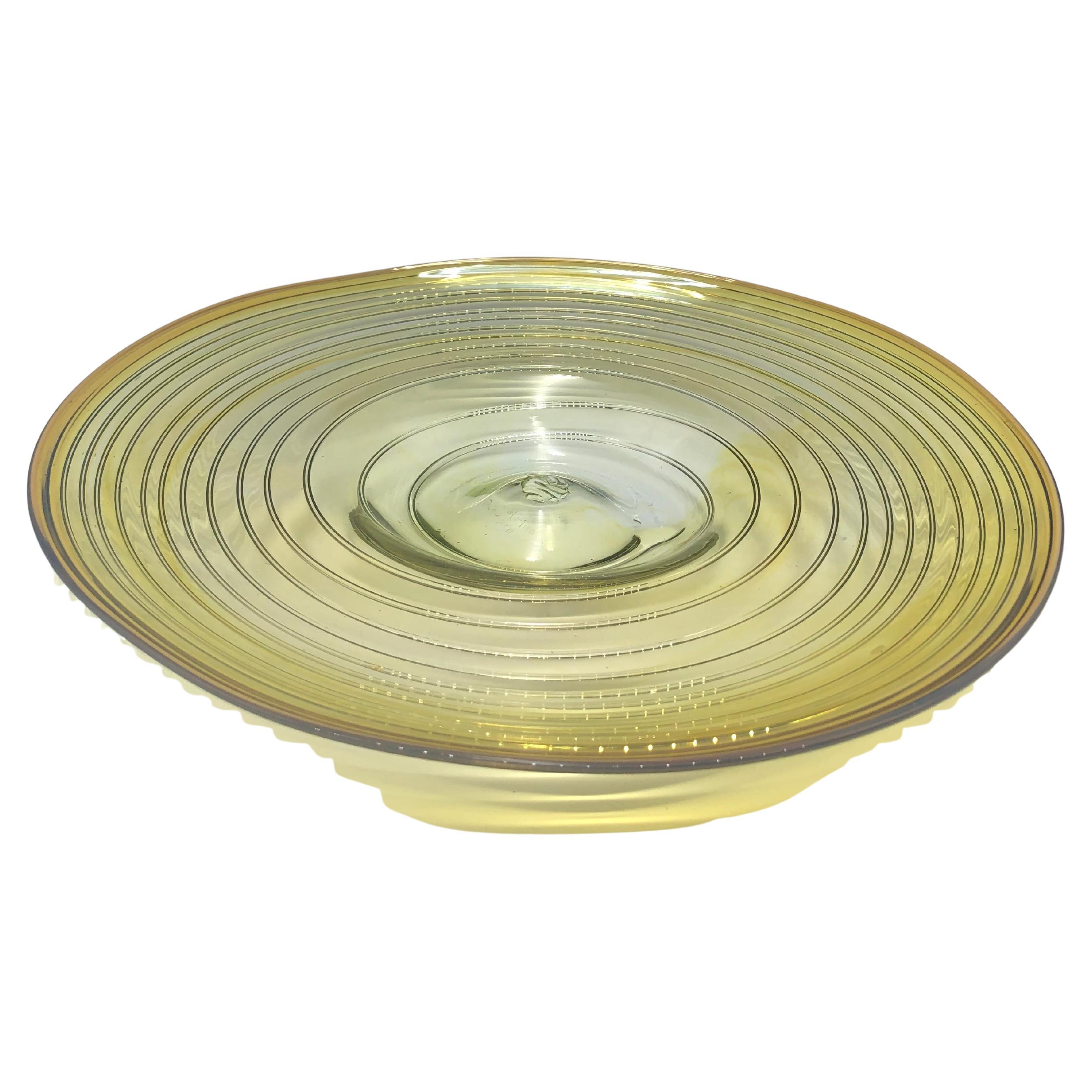 Bellissimo centrotavola in vetro giallo creato da Peter Bramhall, firmato e datato 8/2/80 sulla base. 

Il piatto dal design a vortice ha una forma unica ed è completamente soffiato a mano, lasciando un sottile segno di pontatura sulla base. Il