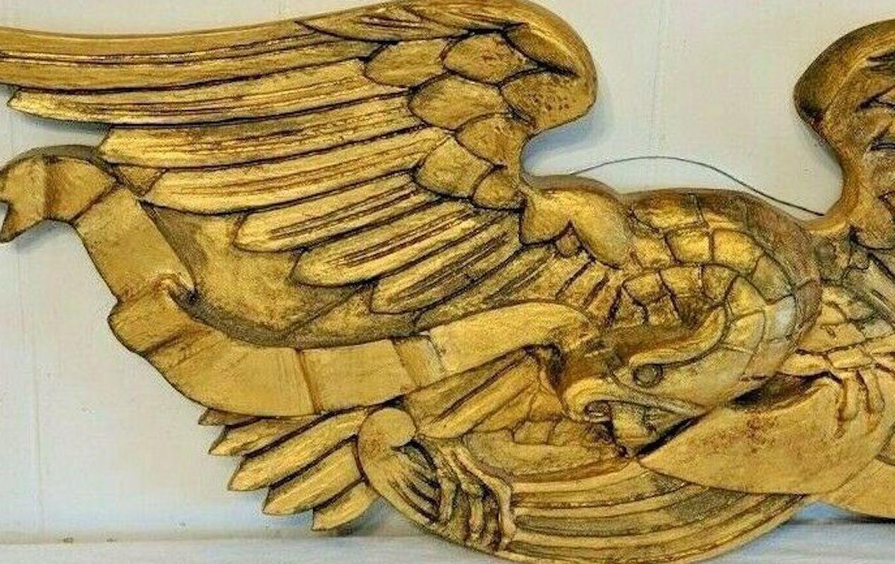 This late 19th to early 20th century wood carved eagle was designed in the style of the famous John Bellamy. Completely gilted, the eagle carries a long, flowing ribbon in its beak. Its wings are spread wide in a presentation style and give the
