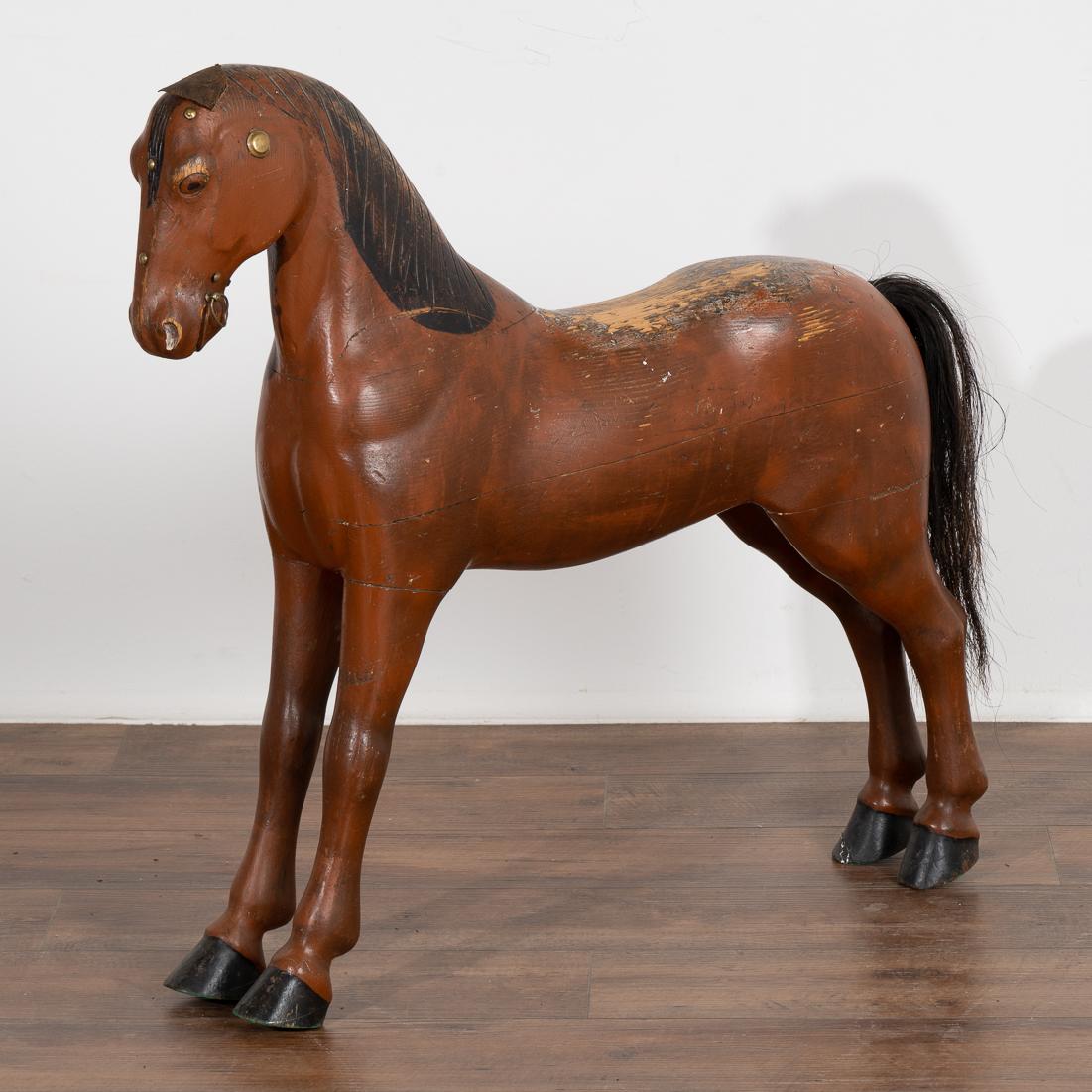 It is the very worn look that creates the wonderful appeal of this original painted and carved horse. 
The brown paint has been worn off along the back, while the tattered leather ears and carved black painted mane reflect a simpler time. Real