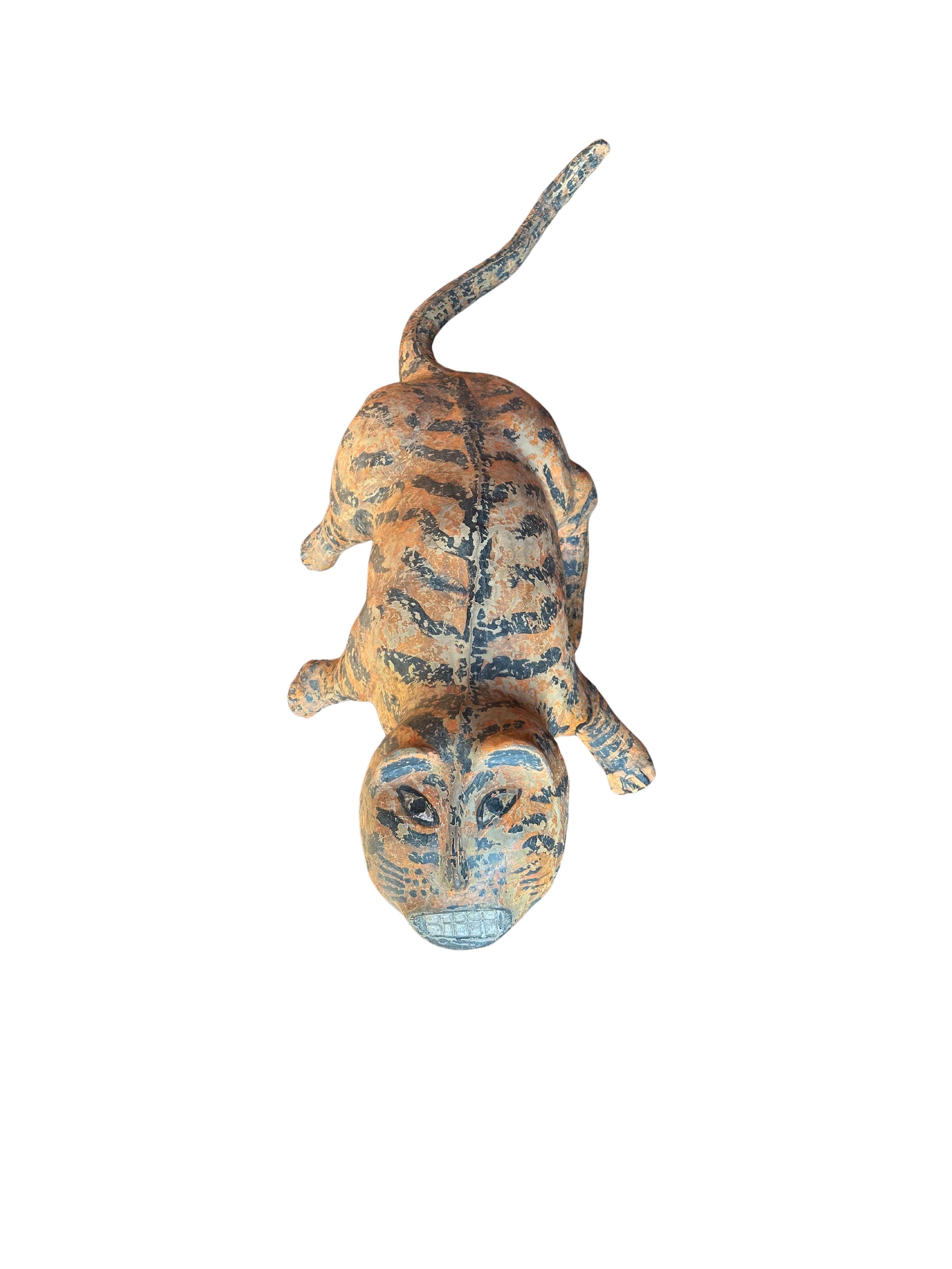 Cette sculpture de tigre vintage sculptée à la main, réalisée dans les riches teintes dorées du bois de jacquier, dégage une qualité intemporelle, presque mythique. Les traits exagérés du tigre - visage large, grands yeux et rictus denté - lui