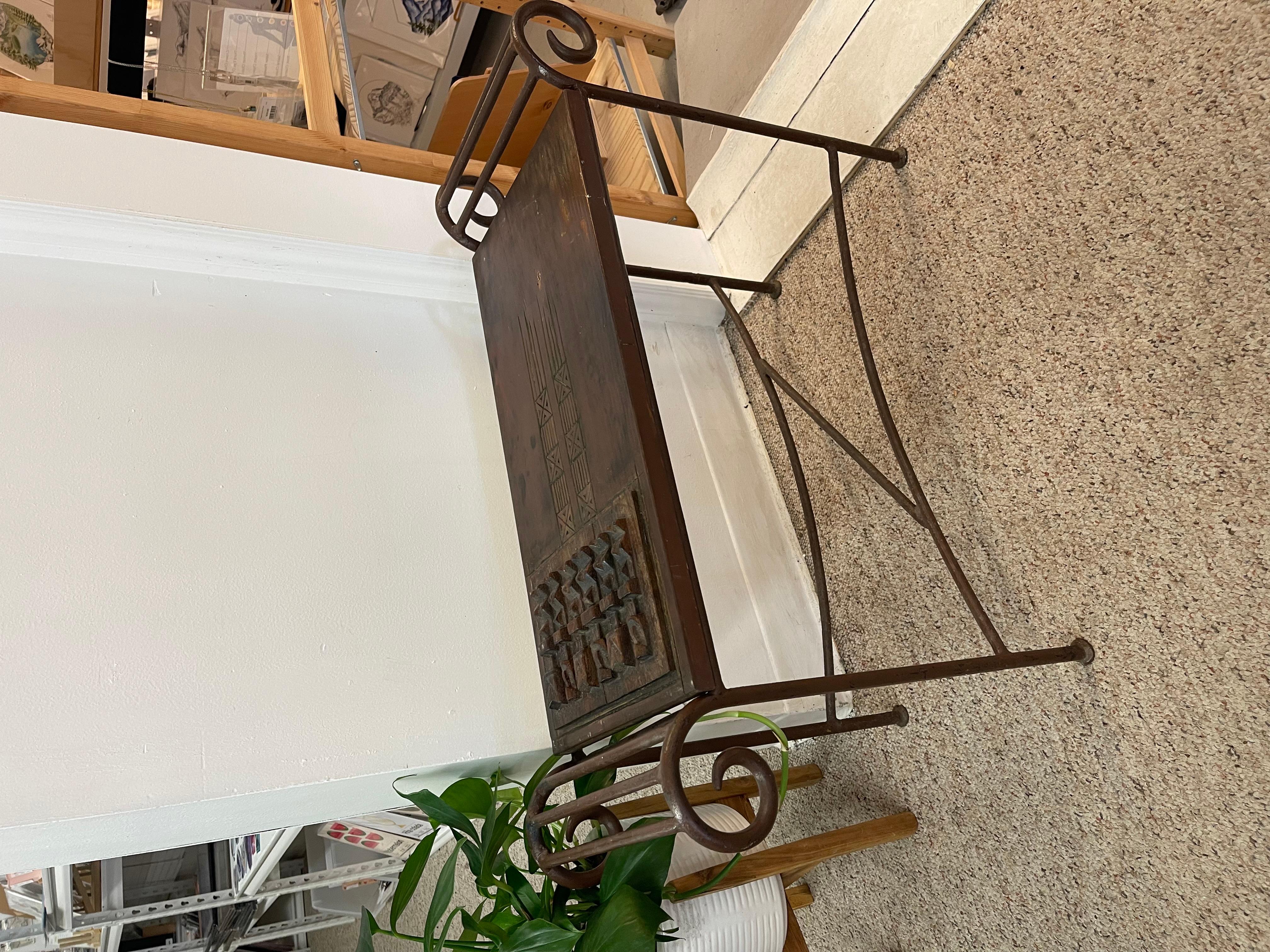 This vintage console table combines rustic craftsmanship with global design influences, featuring a hand-carved hardwood top and a sculptural wrought iron base. The tabletop is inset with a deeply carved panel showcasing a grid of abstract,