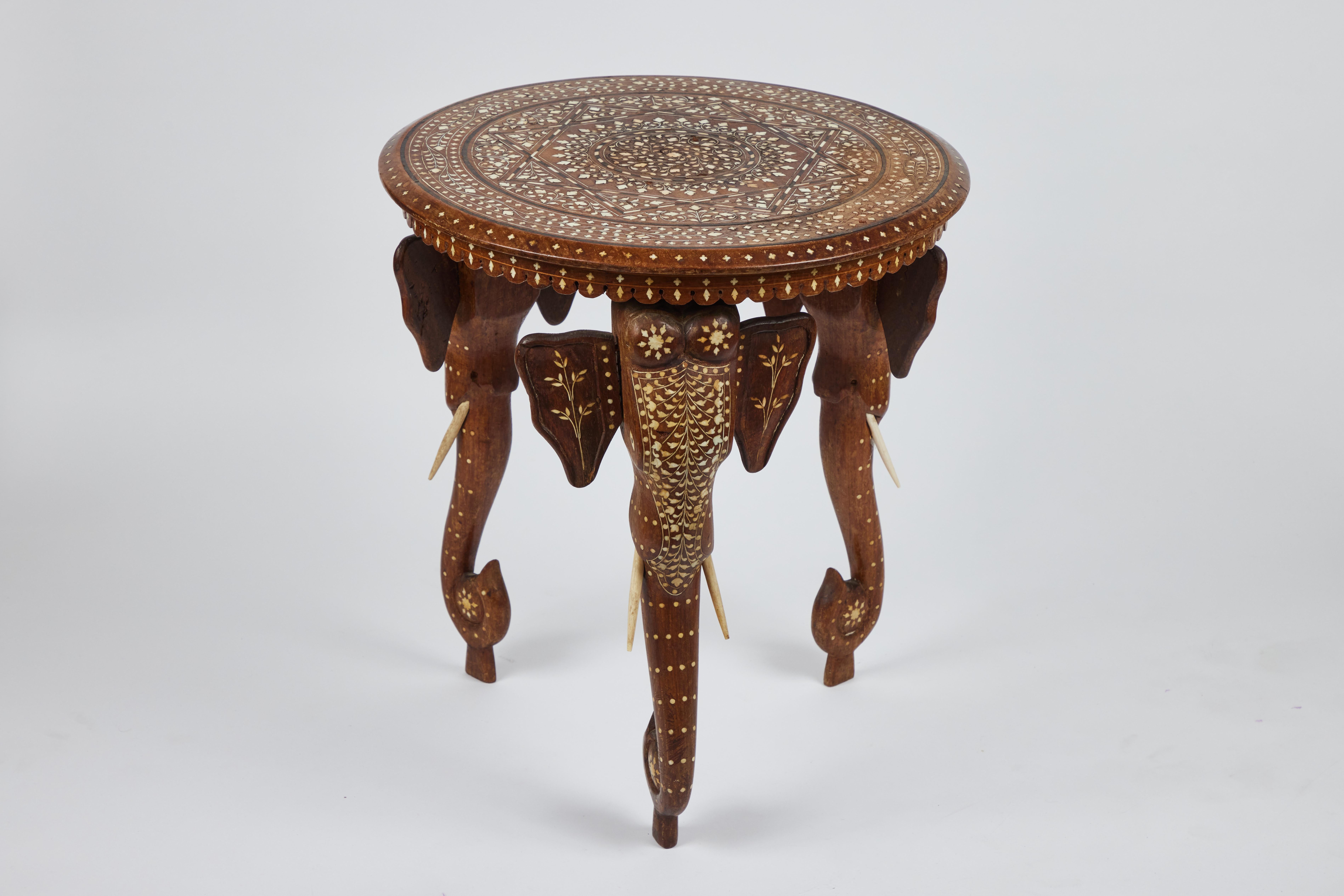 A detailed vintage hand carved wood side table with 'elephant head legs' and intricately inlaid bone designs all over the top and legs. It is made in British India.

Measures: 18