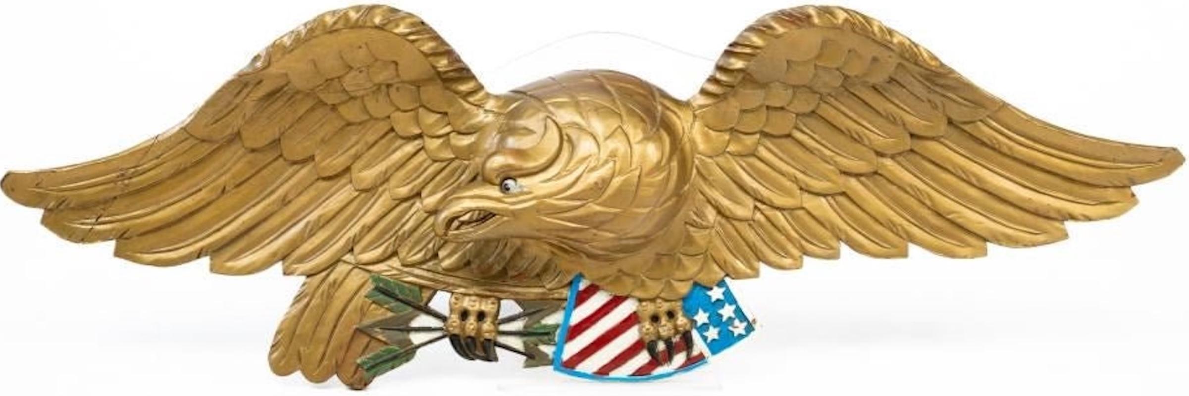 Presented is a vintage, Bellamy-style, hand-carved wooden eagle. This early 20th century wood eagle is gilded with a painted red, white, and blue shield. It supports a patriotic shield in its right talon as the head looks to its left. The clutched