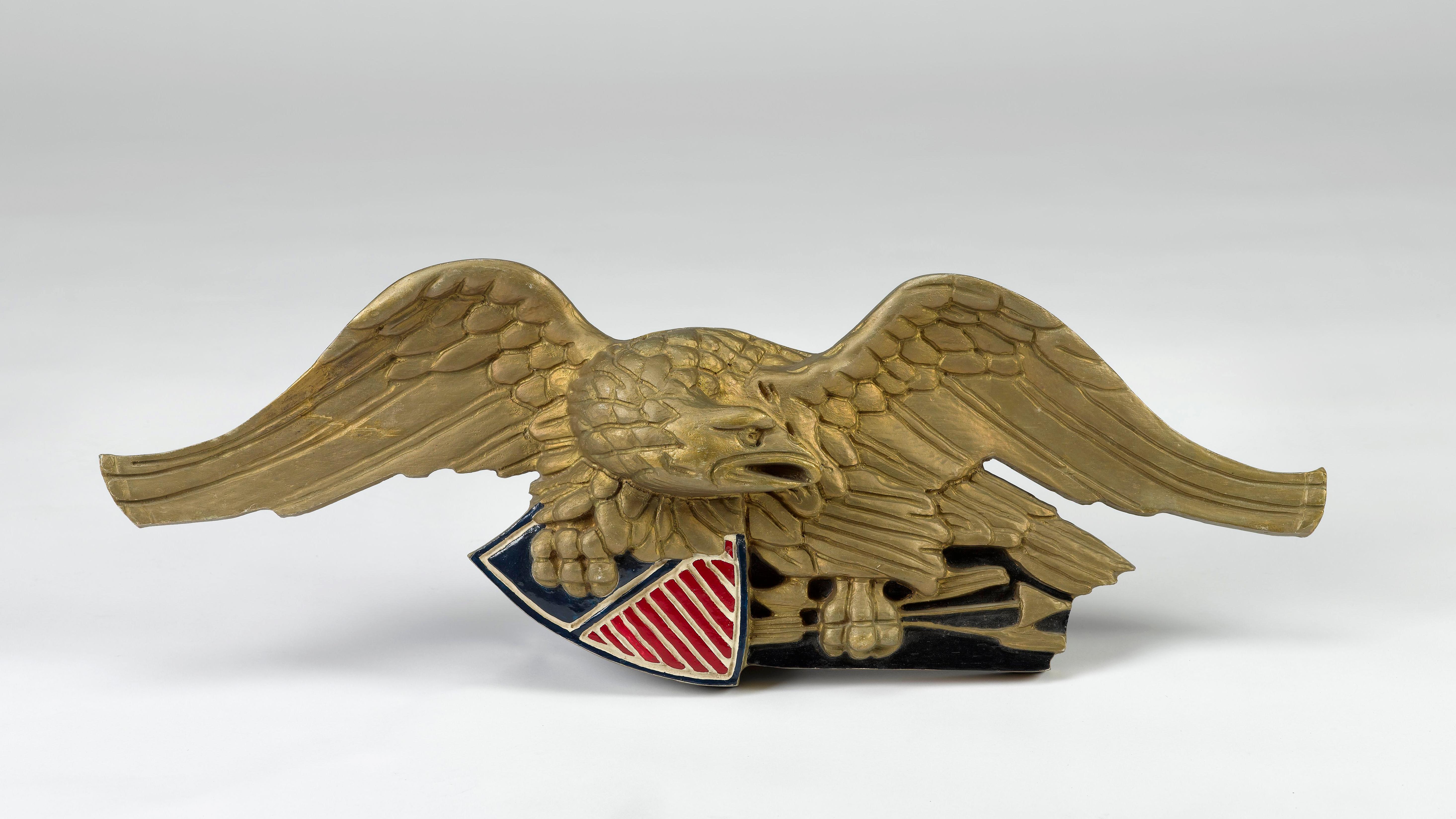 Presented is a vintage, Bellamy-style, hand carved wooden eagle. This late 19th century to early 20th century wood eagle is bronze-brushed with a painted red, white, and blue shield. It supports a shield in its right talon as the head looks to its