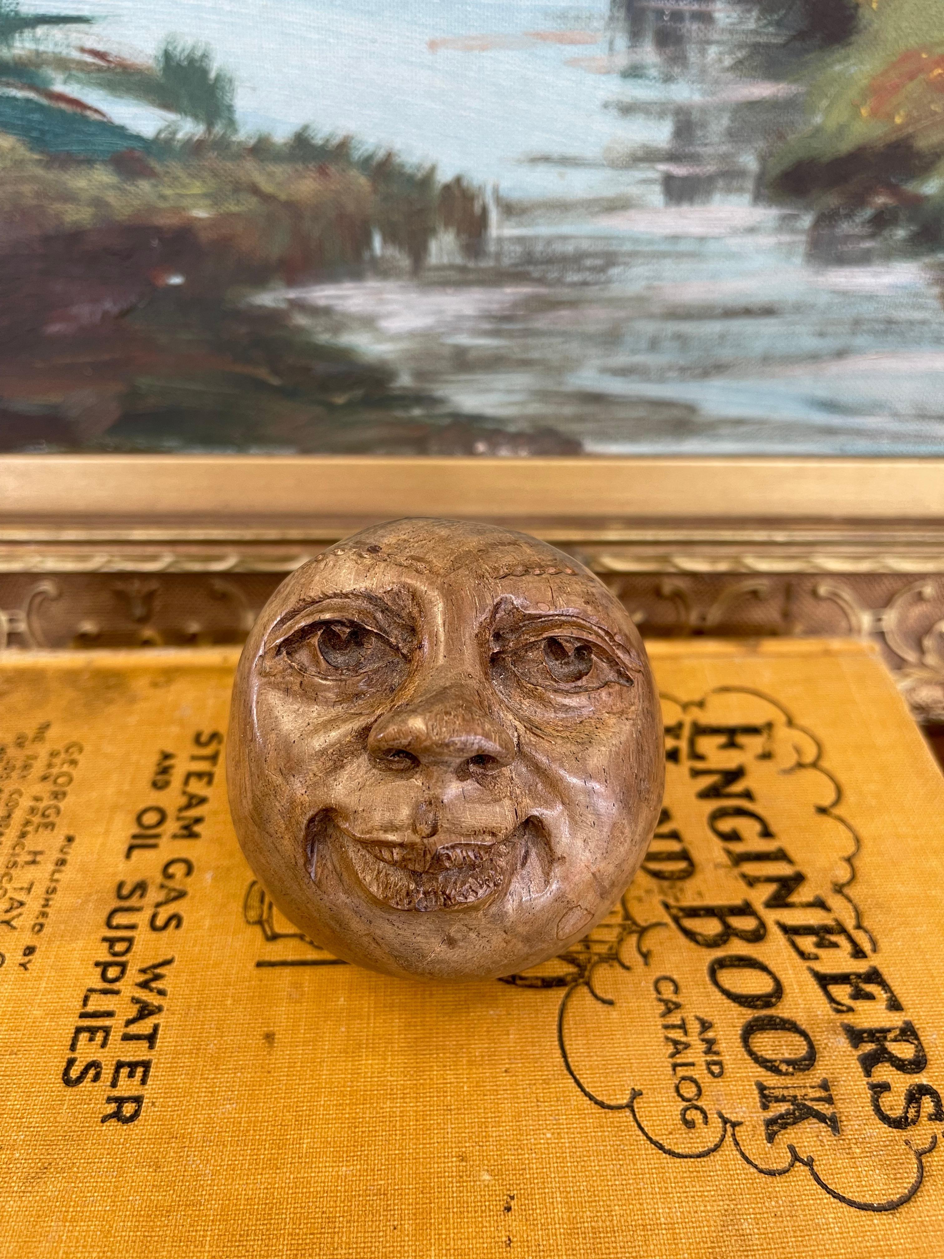 Questa stravagante scultura in legno vintage presenta un volto di luna sorridente intagliato a mano e reso ricco di dettagli. Sapientemente modellato in una forma sferica, il volto espressivo mostra occhi profondi, sopracciglia arcuate e un sorriso