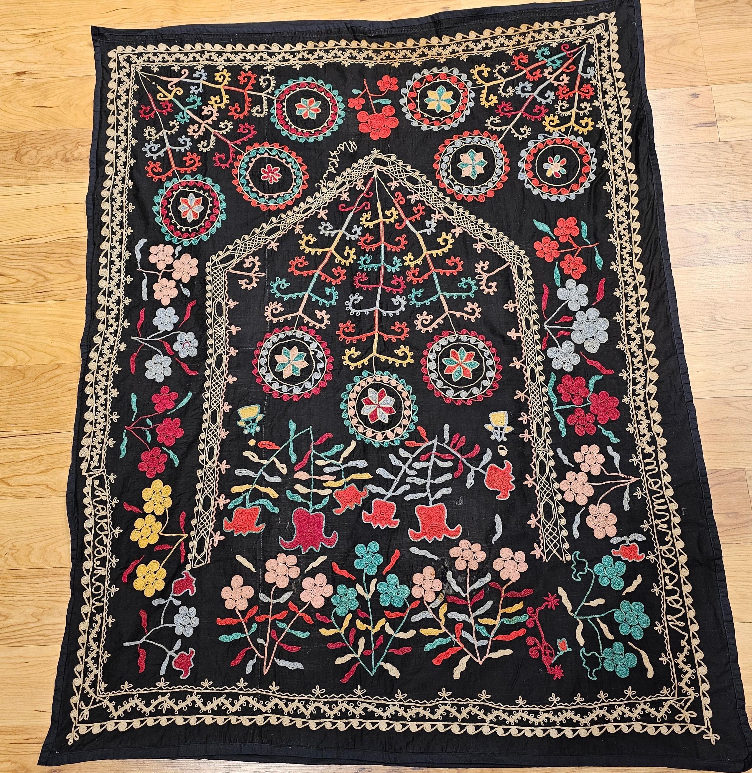 Vintage hand-stitched Suzani silk embroidery from Uzbekistan in Central Asia in a “Prayer Rug” pattern.  The vintage Uzbek Suzani is on a black cotton background with silk embroidery in red, blue, green, yellow.    The design of this Suzani