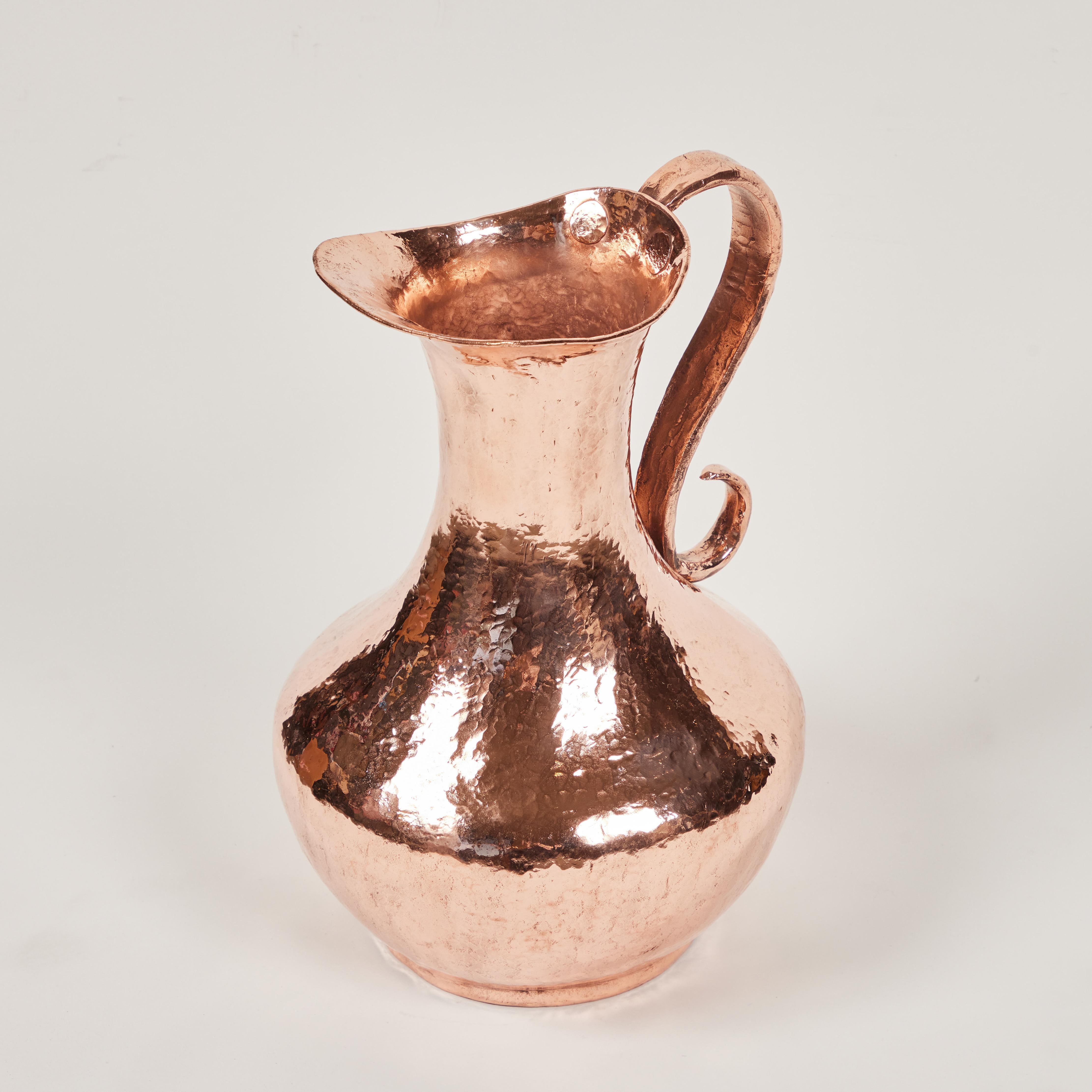 This large and striking vintage copper pitcher has been hand-forged, hammered 
and adorned with its own dramatic signature 'S' handle. It has been newly polished and is the perfect accent or centerpiece on any table.

It measures 10.5