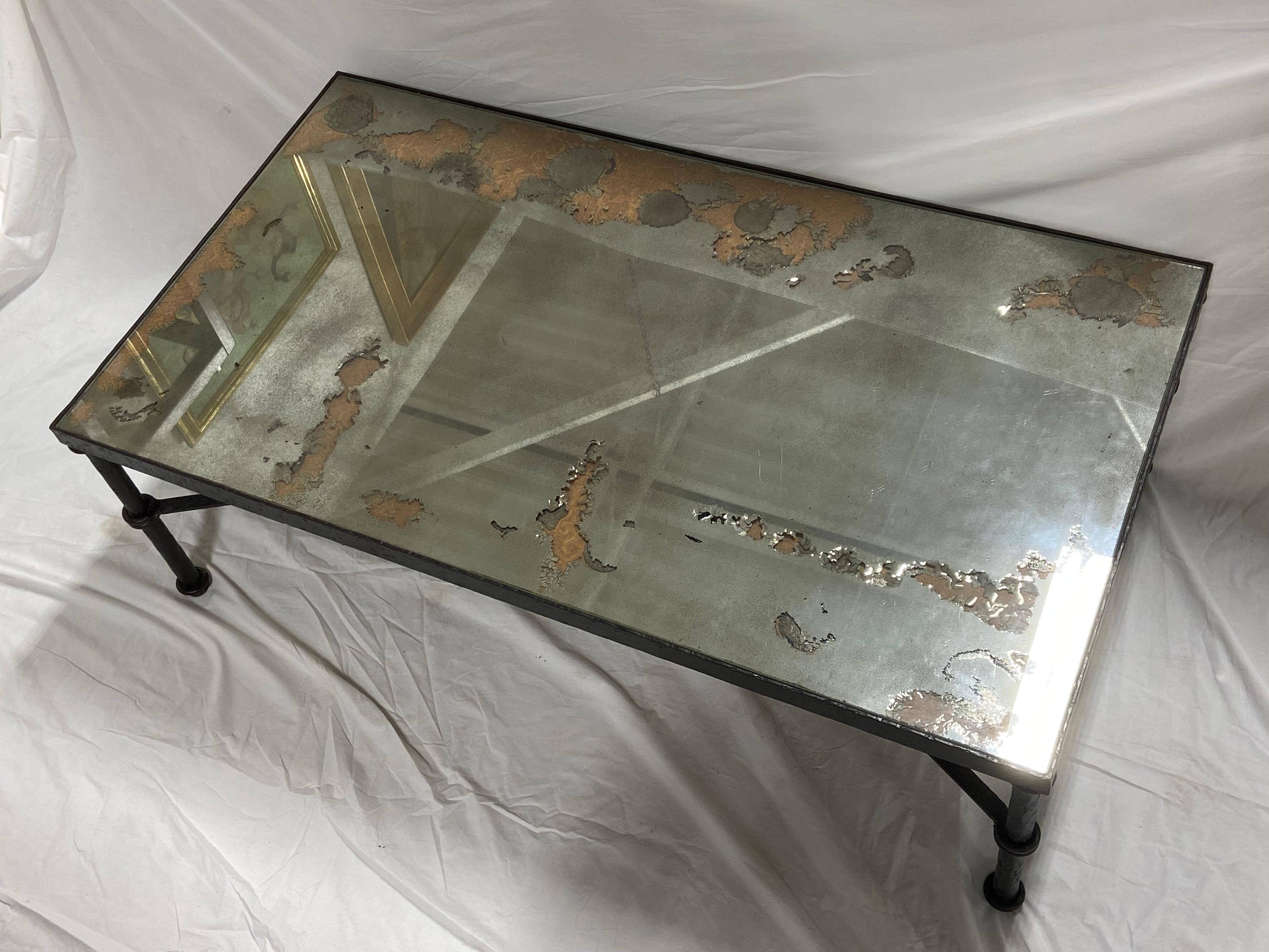 A large vintage iron coffee table with a hand hammered style finish as well as a distressed / aged mirror top. The table is in the style of works by Diego Giacometti. Through the distressed mirror top in certain areas, the backing support is