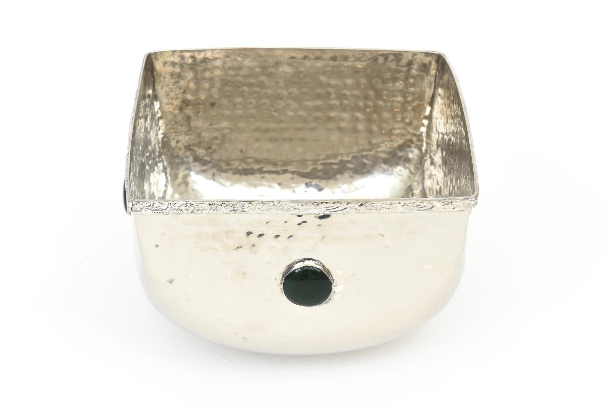 This lovely vintage large hand hammered silver-plate bowl has a lip rim and base of a flowered fleur de lis design surround of some sort. There are 4 glass stones of dark blue and dark green on the perimeter; 2 of each. it is not marked anywhere. We