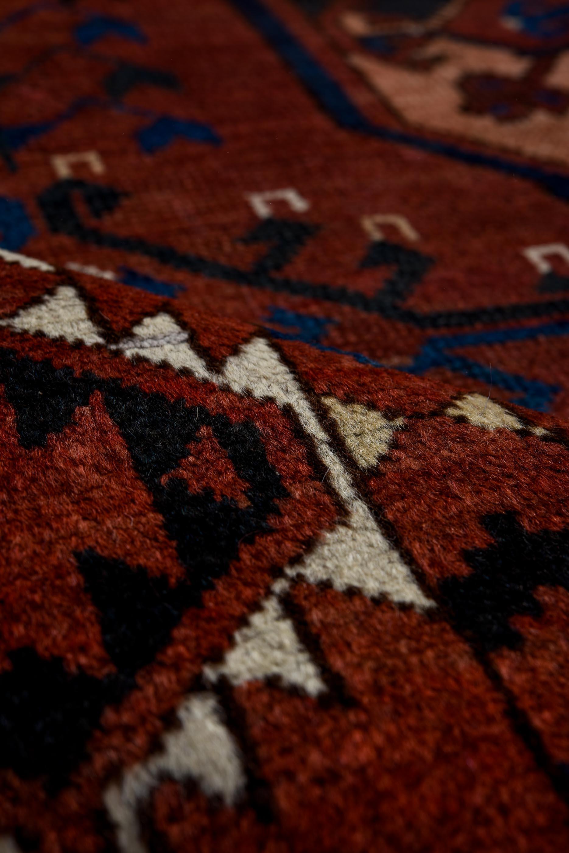 This vintage Afghan rug features a striking allover arrangement of classic octagonal gul medallions set against a rich madder red field. Deep indigo, warm camel, and touches of lapis and ivory accent the bold geometry, reinforcing the tribal