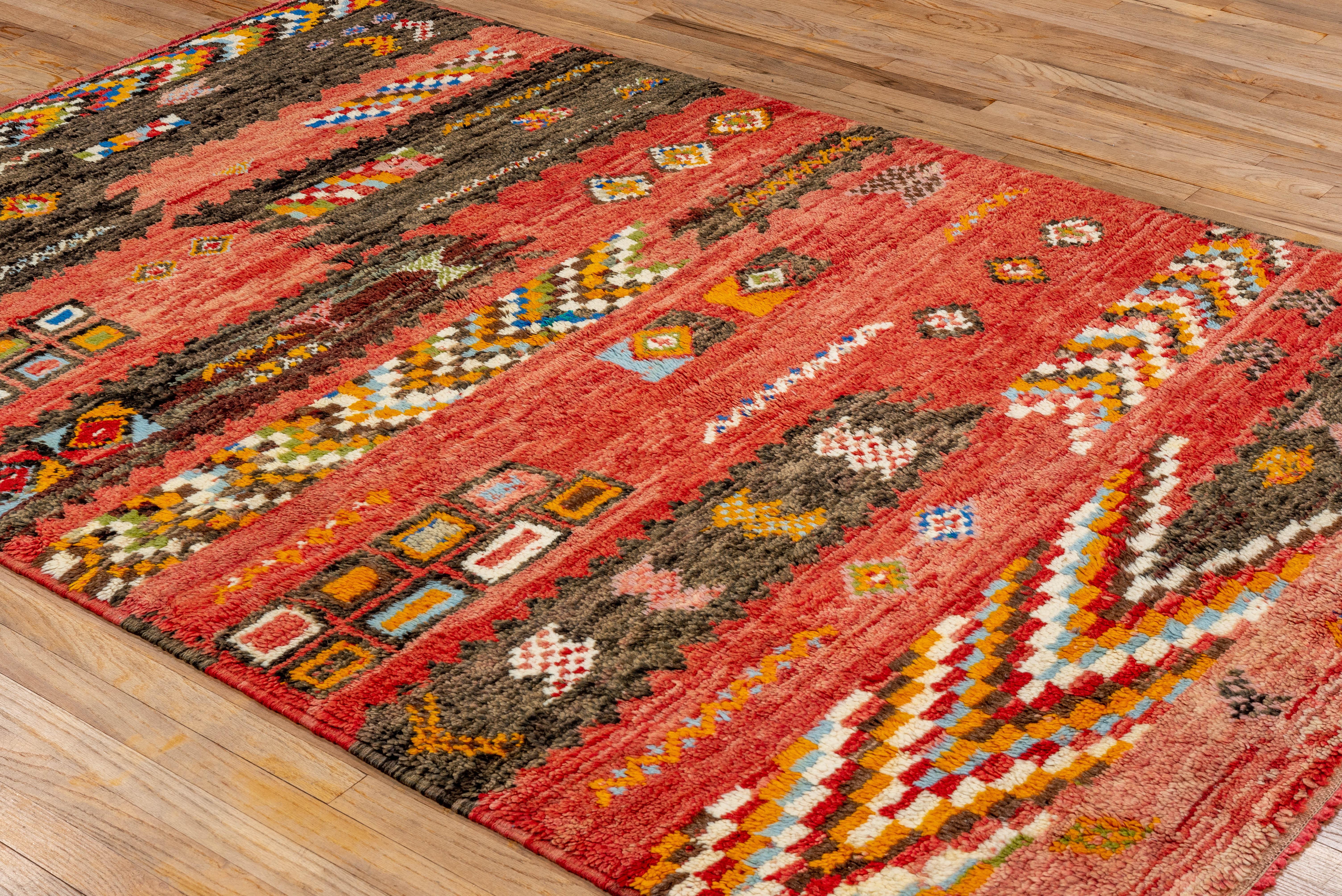 Bursting with energy, this vintage Moroccan rug showcases a playful composition of abstract tribal forms on a vivid red and charcoal field. Hand-knotted with wool, it blends bold color blocking, checkered bands, and scattered diamond motifs into a