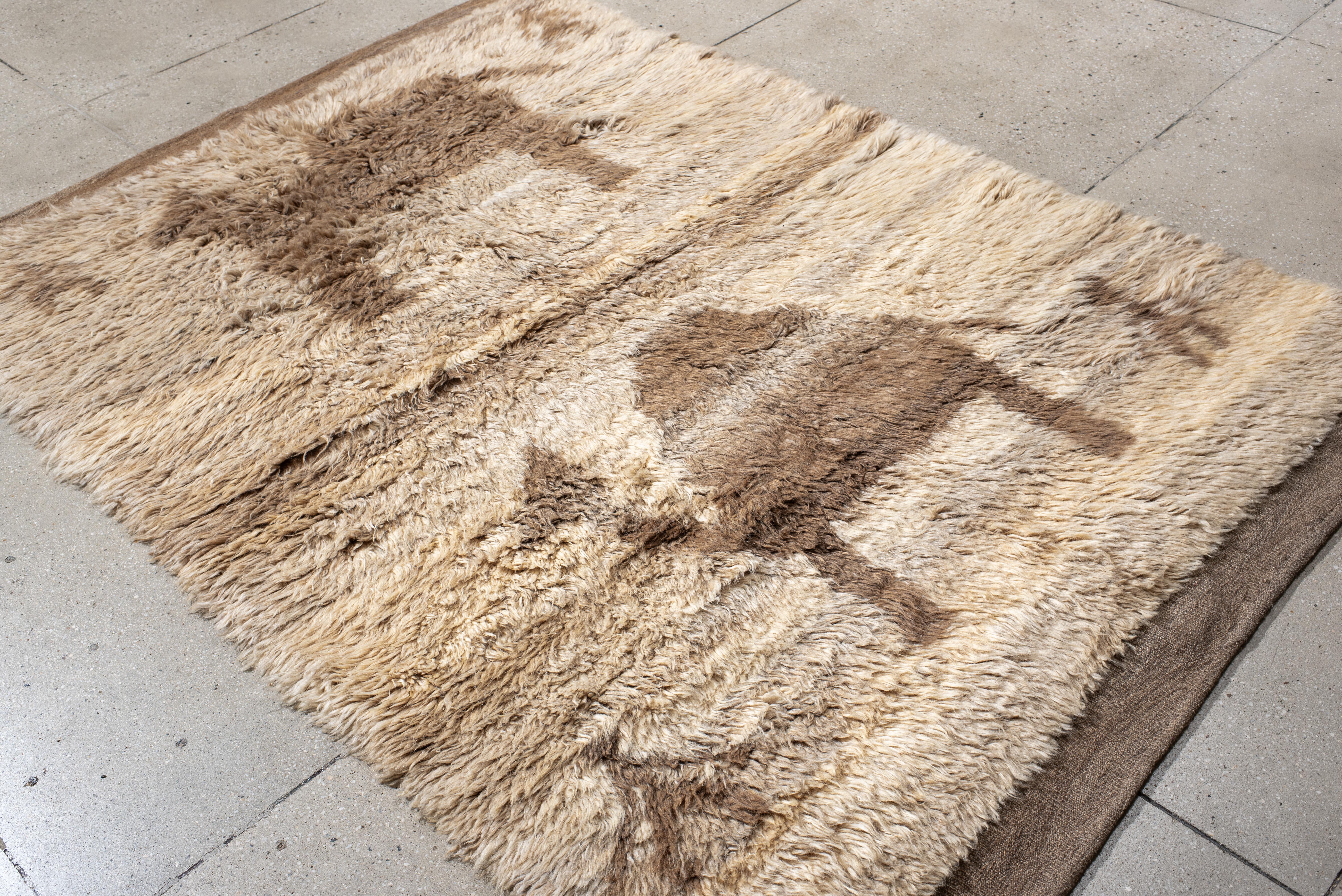 This vintage Moroccan rug captures the spirit of desert life through its charming camel and figure motifs, hand-knotted in a warm, tonal palette of sandy beige and soft taupe. The thick, plush pile offers inviting texture, ideal for grounding a