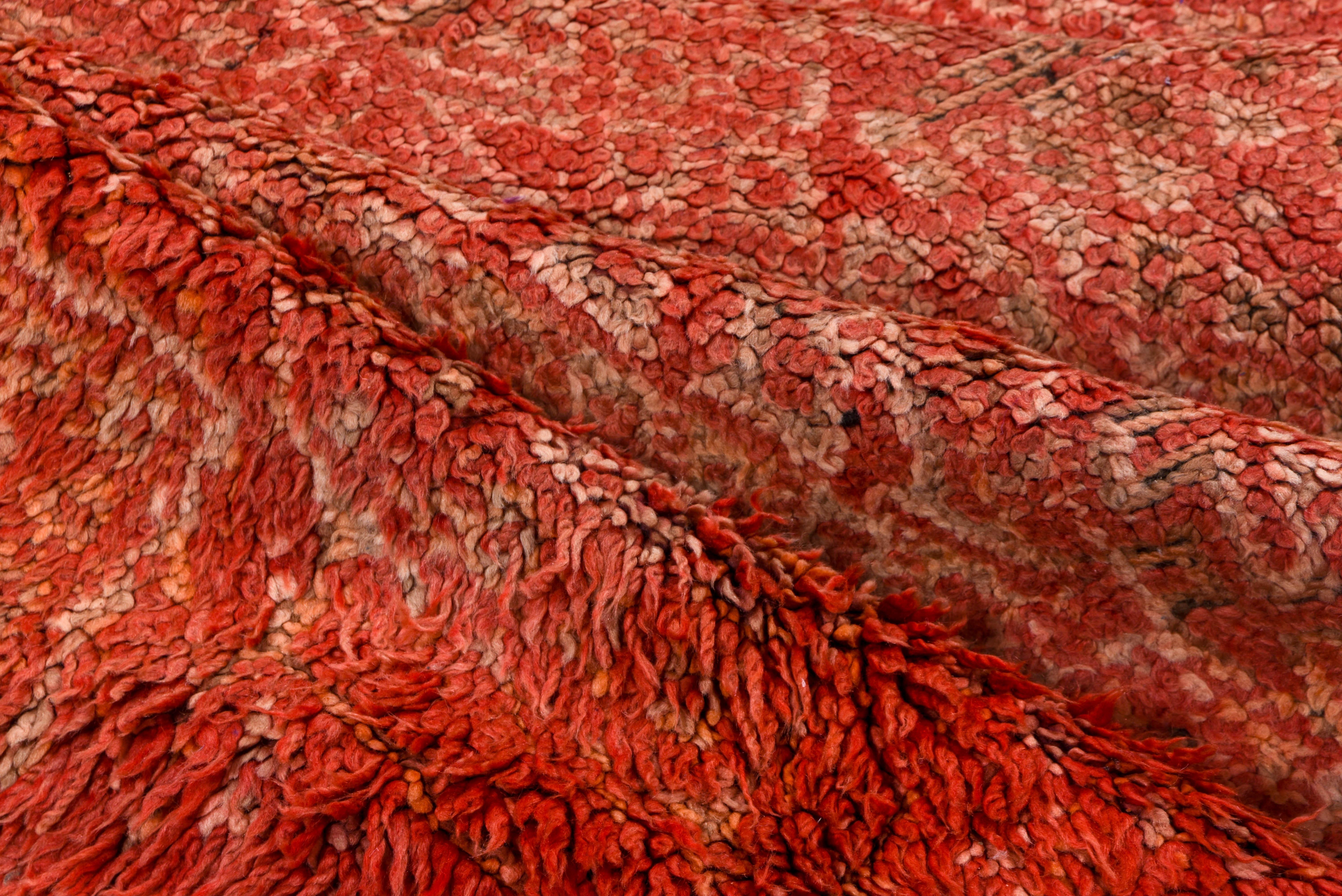 This vintage Moroccan rug features a richly faded crimson field with intricate geometric detailing subtly woven into its surface. Dark borders frame the composition, adding structure to its worn, time-softened aesthetic.
