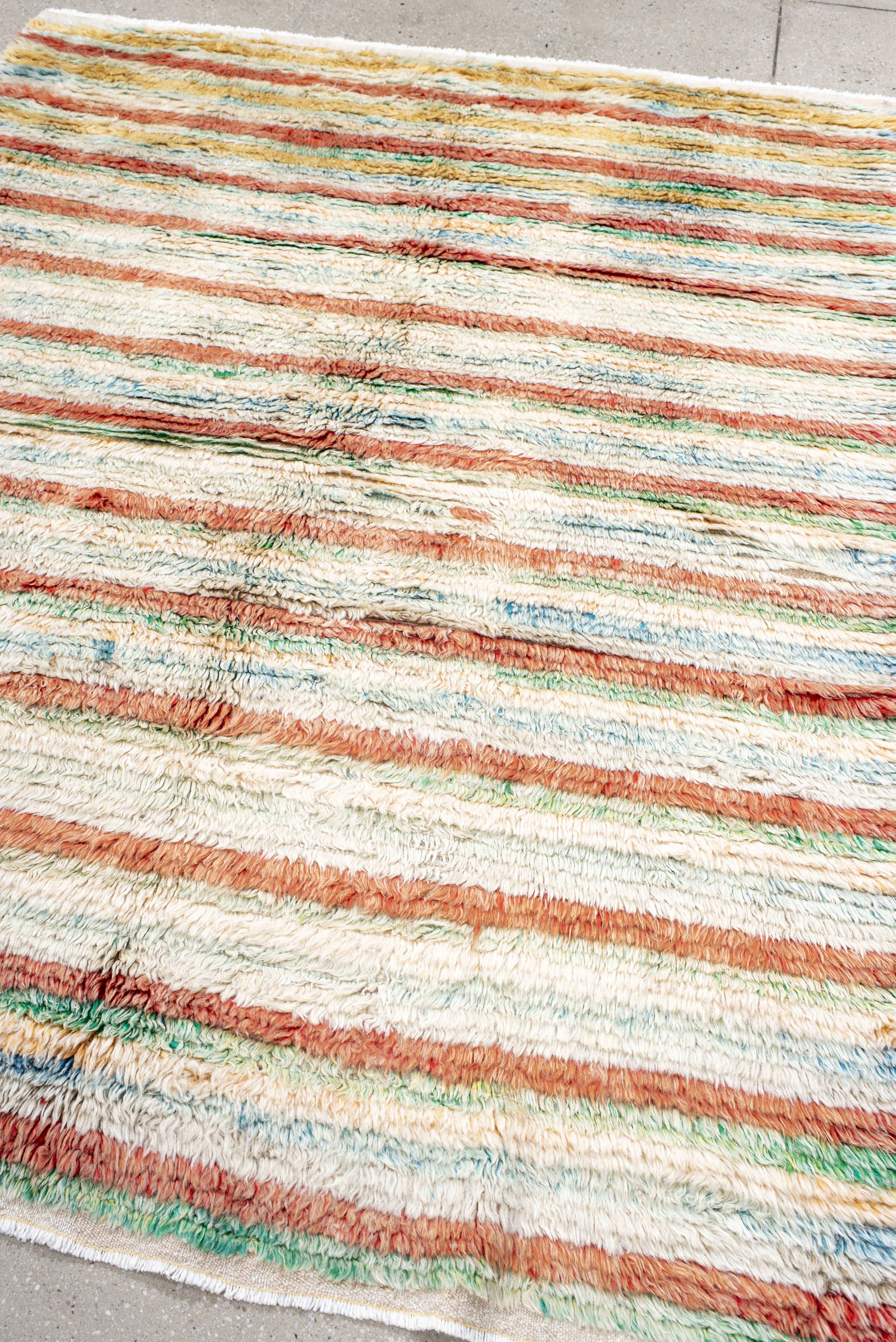 Dieser marokkanische Teppich im Vintage-Stil fängt mit seinem sanft getönten horizontalen Streifendesign den Geist moderner Bohème-Einrichtungen ein. Handgeknüpft mit einem dicken, plüschigen Flor, zeigt er eine cremefarbene elfenbeinfarbene Basis,